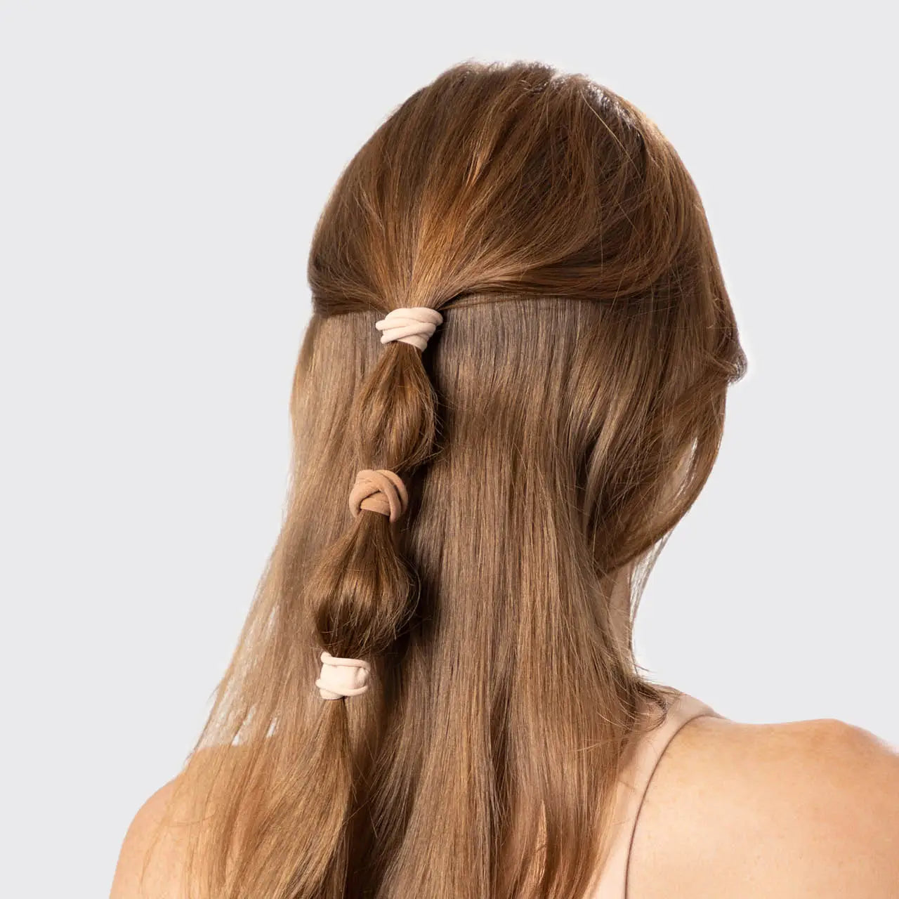Long brown hair styled in a half-up, half-down look with pink hair ties on a light gray background