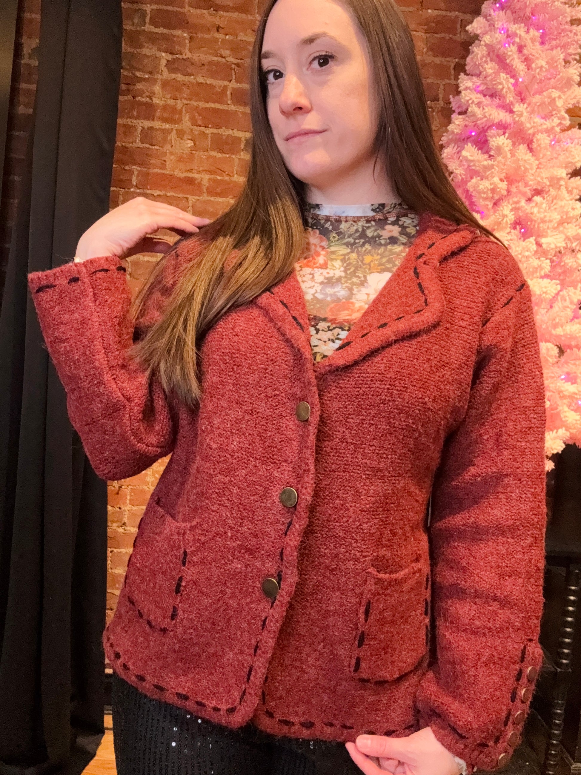 A woman wearing a red blazer with a classic pattern, featuring long sleeves, stitch detailing, lightly padded shoulders, and decorative gold buttons.