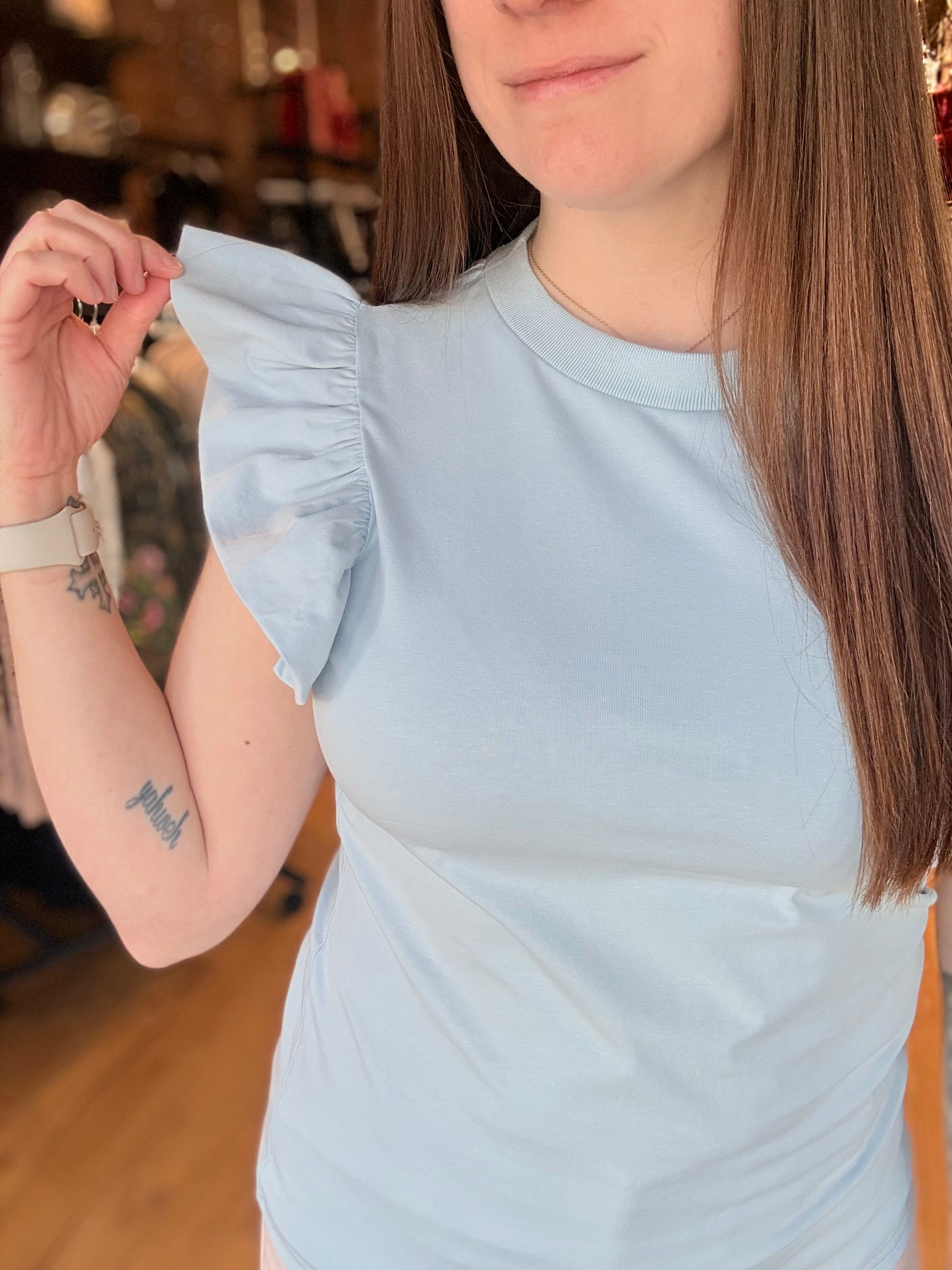 Woman wearing a light blue top with ruffled sleeves in an indoor setting.