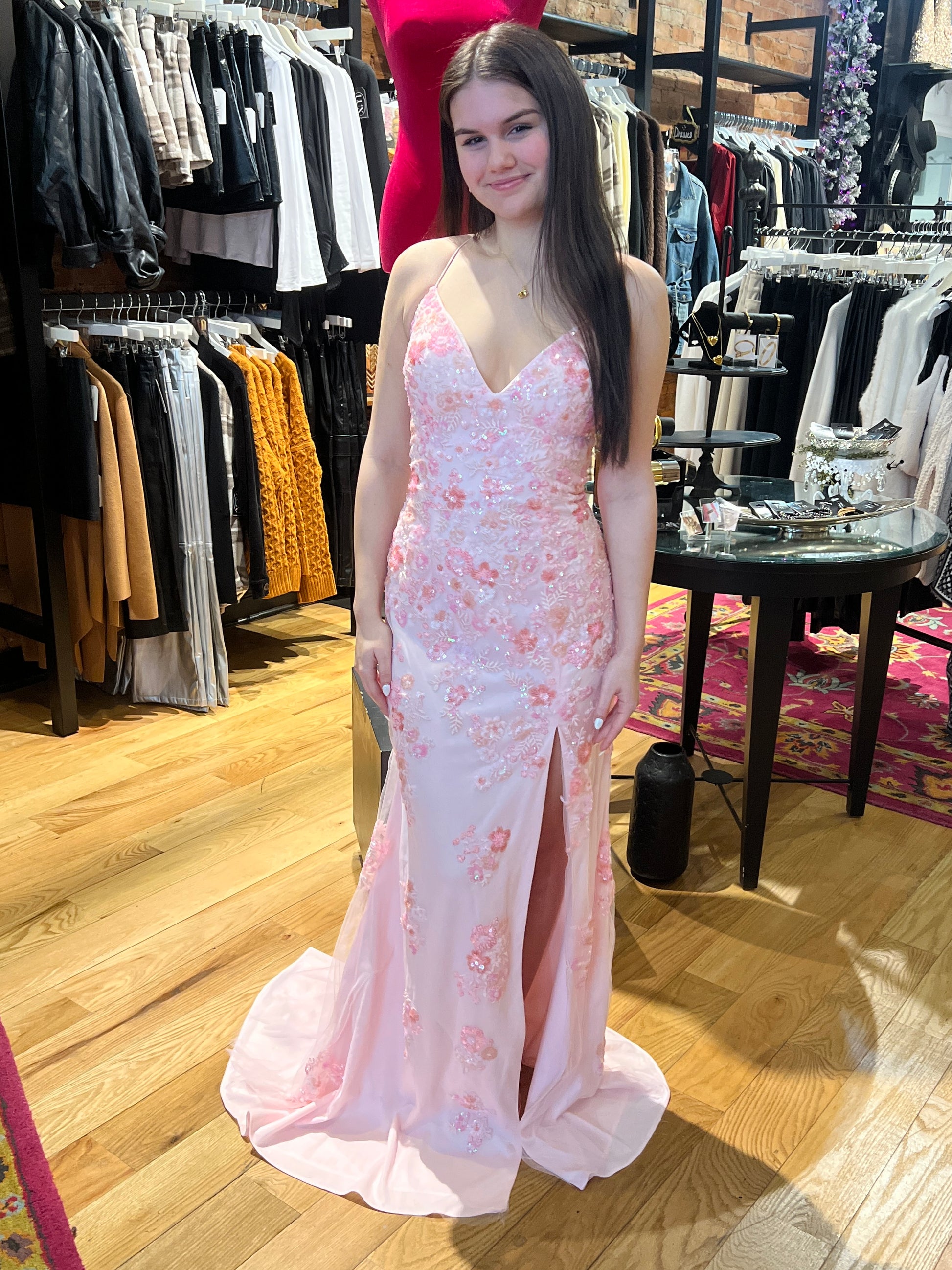 Woman in a pink floral evening gown standing in a clothing store.