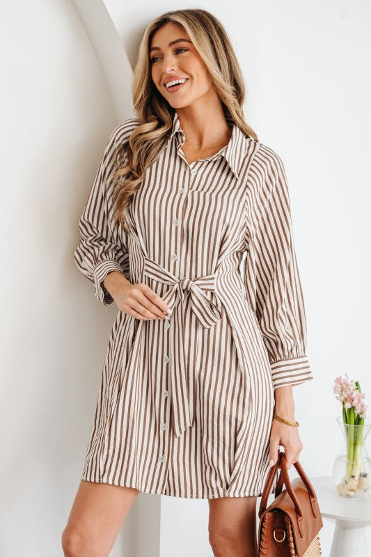 Woman wearing a striped shirt dress with a white wall background