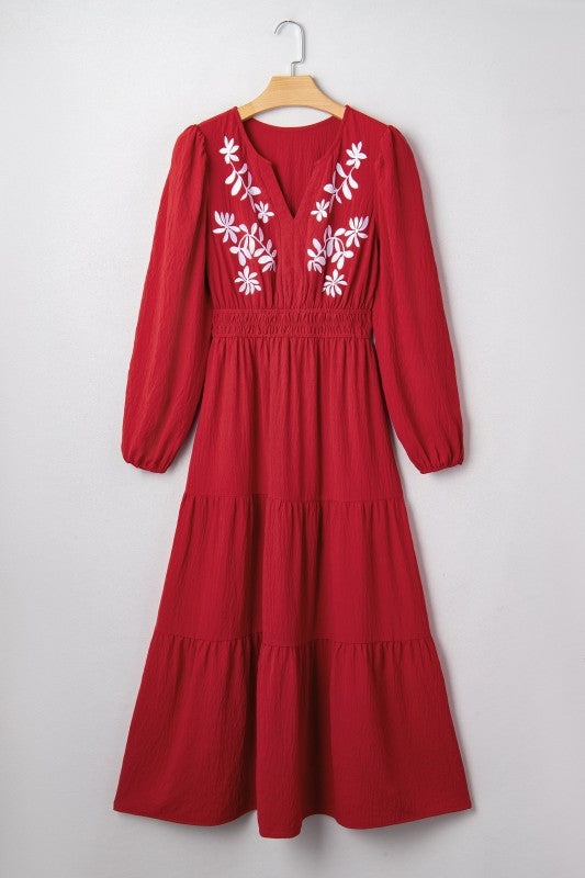 Red dress with white floral embroidery on a hanger against a white background