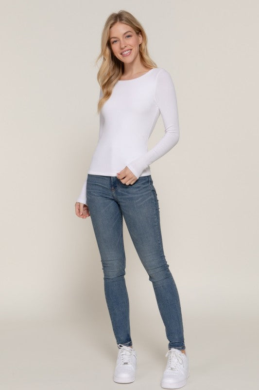 Woman wearing a white long-sleeve top and blue jeans on a beige background