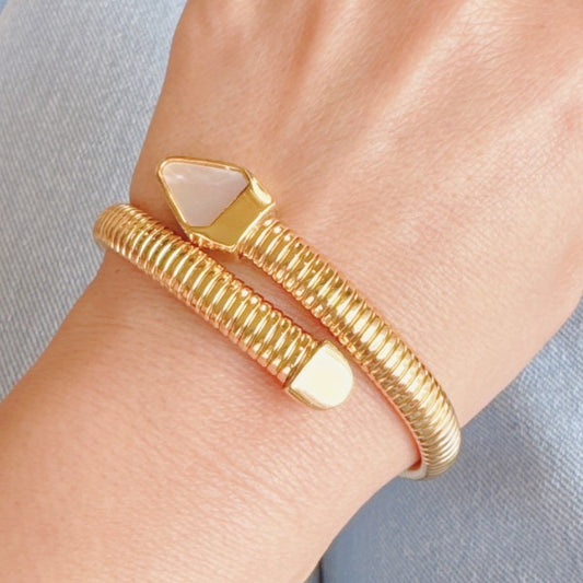 Gold bracelet with geometric design on a wrist against a light gray background