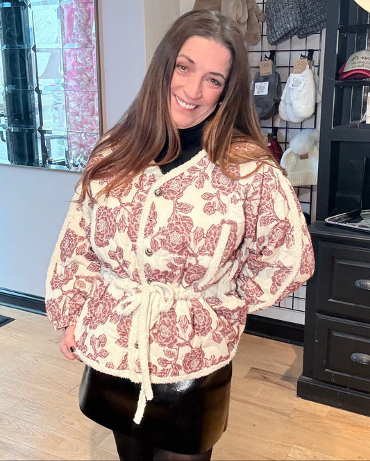 Woman wearing a patterned dress in a store setting with clothing racks and hats.