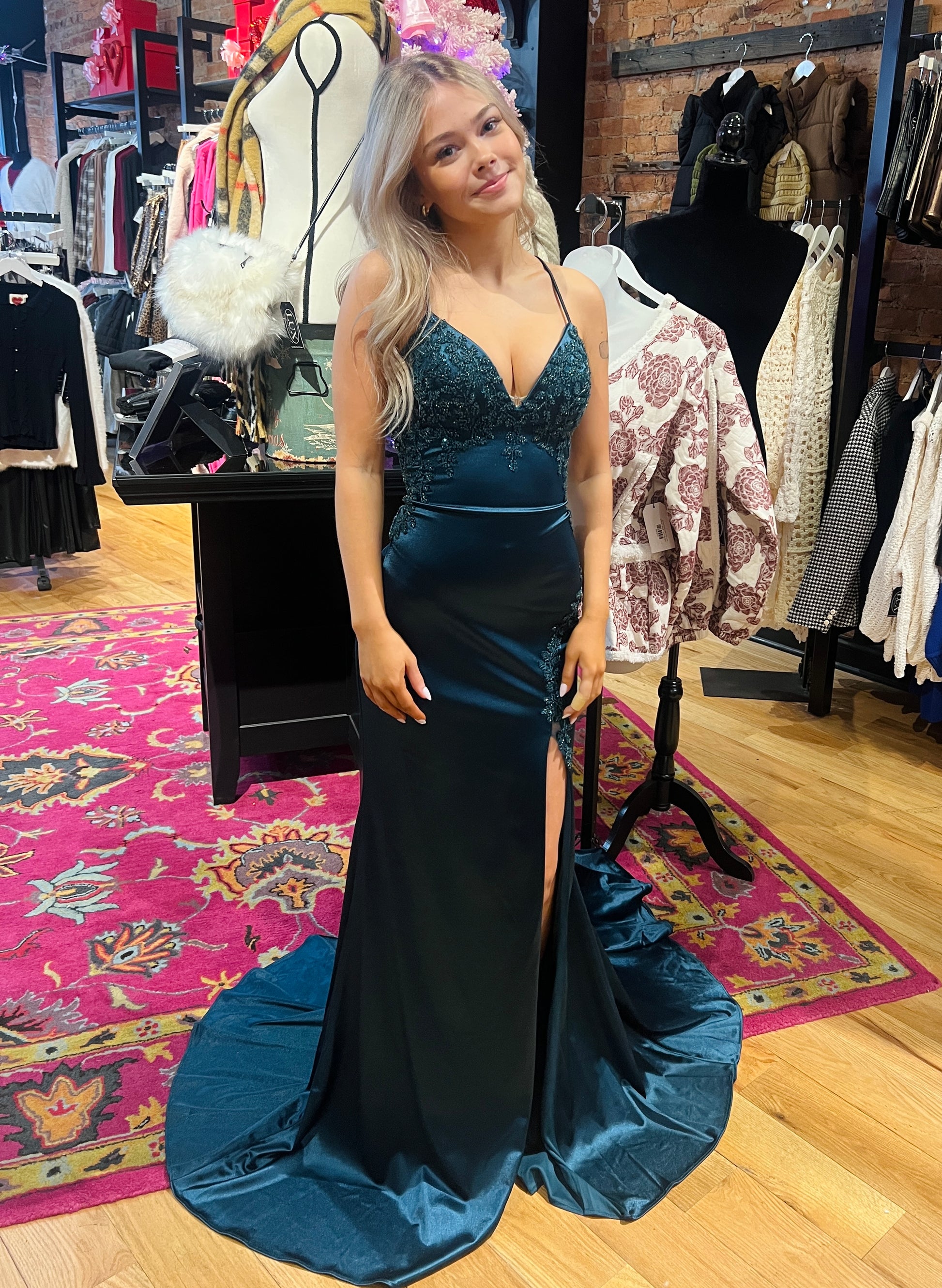 Woman in a blue evening gown holding a matching clutch in a clothing store.