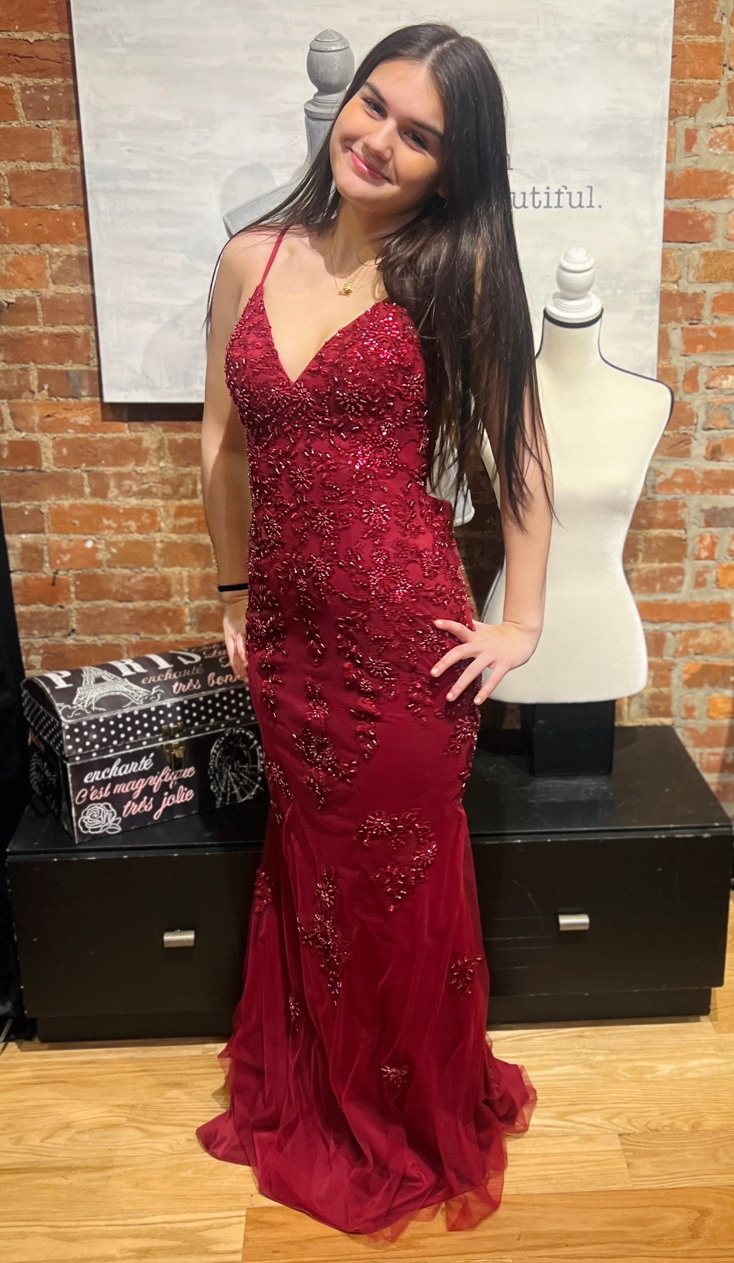 Woman in a red evening gown standing in front of a brick wall with mannequins.