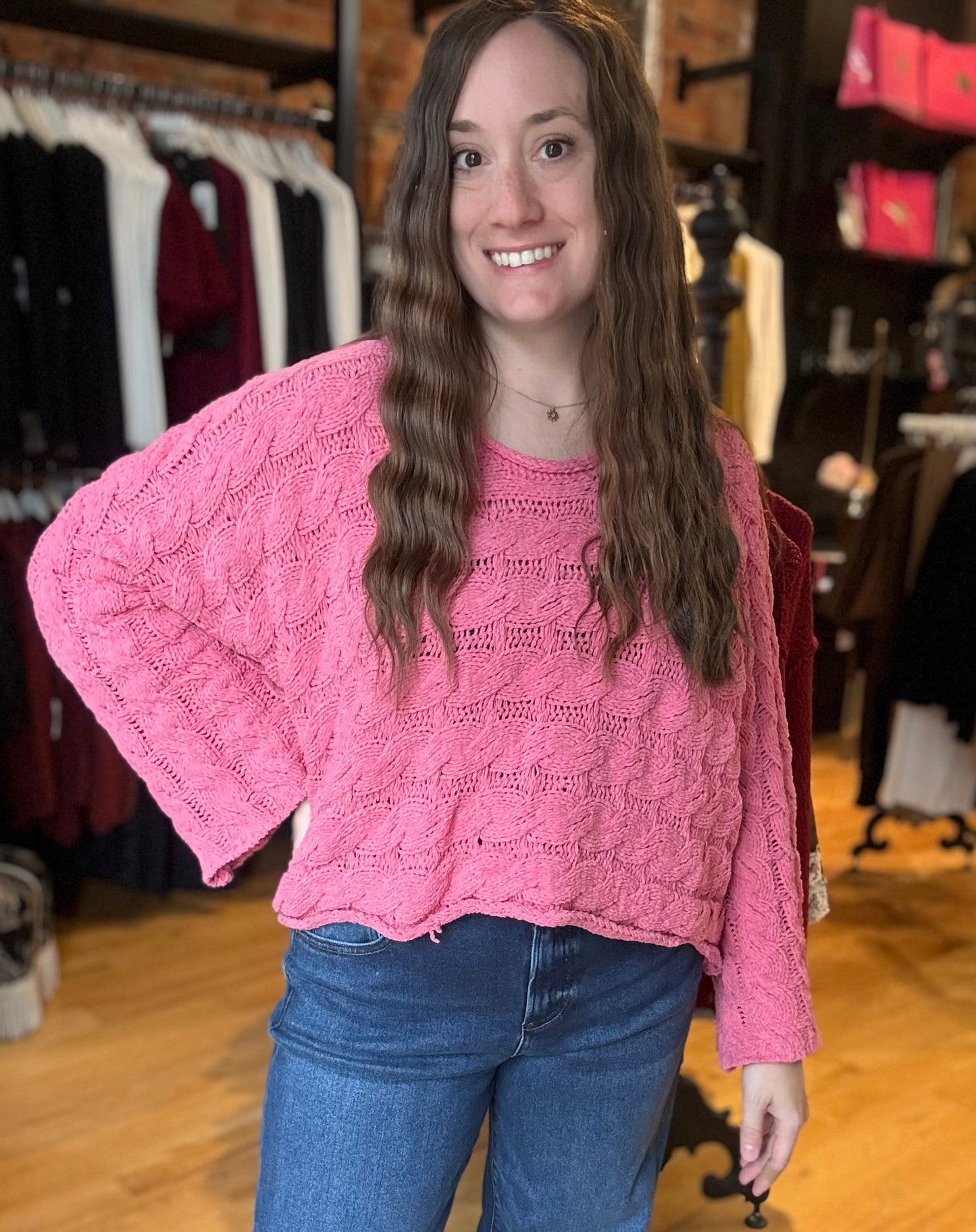 Woman wearing a pink sweater and blue jeans in a clothing store.