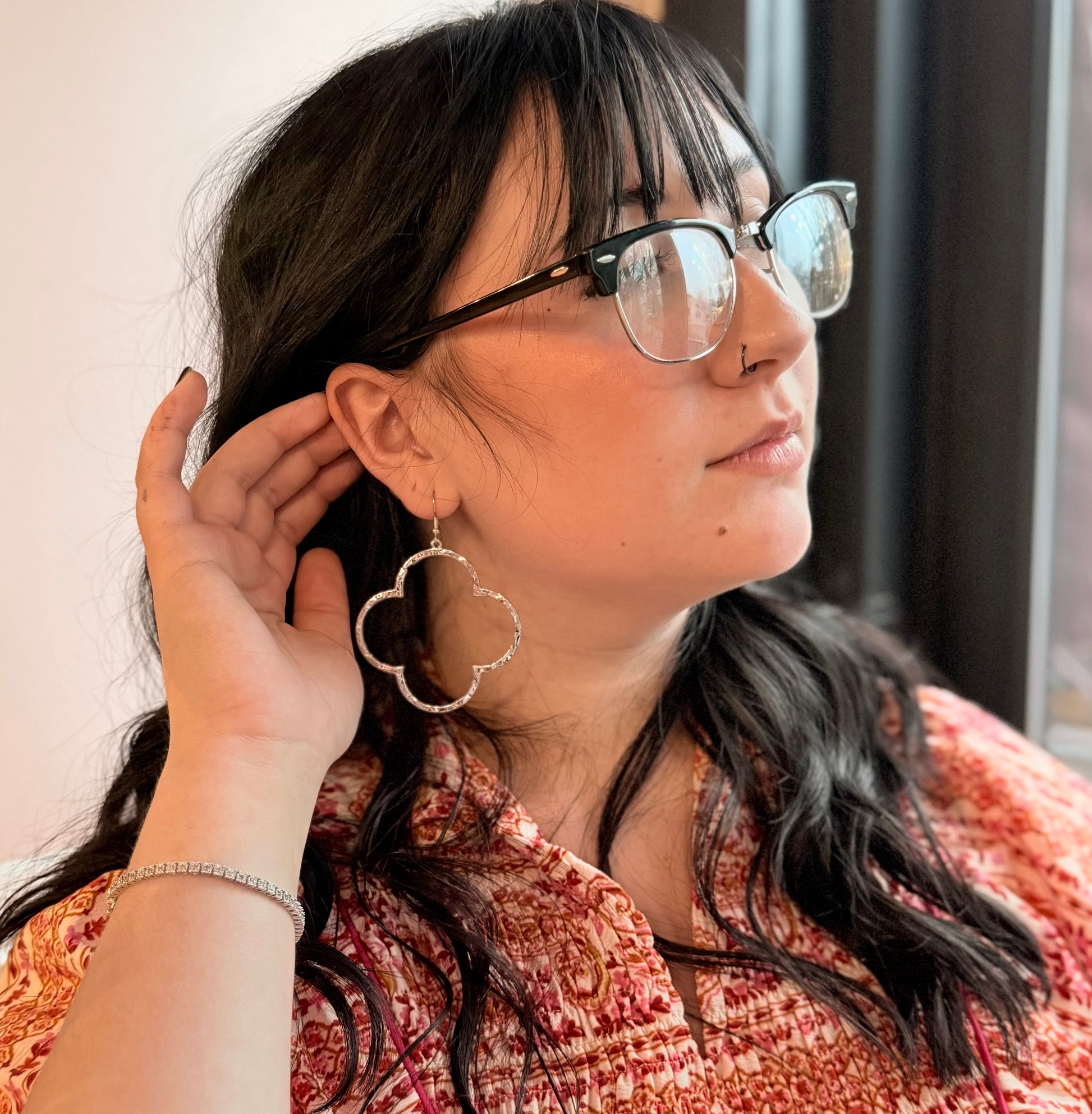 A person wearing the Covered in Clover Hoop Earrings, which are gold or silver-plated alloy earrings with a clover design.