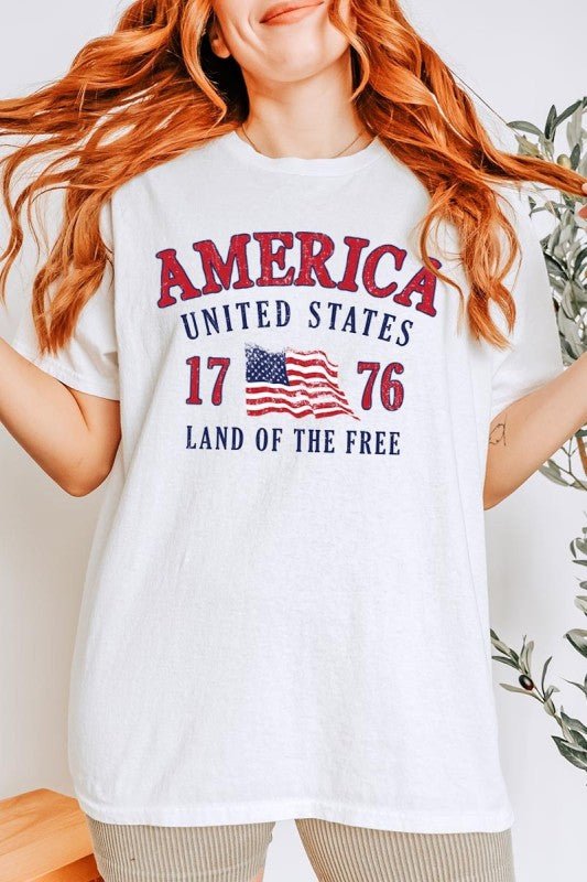 Person wearing a white t-shirt with 'America United States 1776 Land of the Free' text and American flag design.