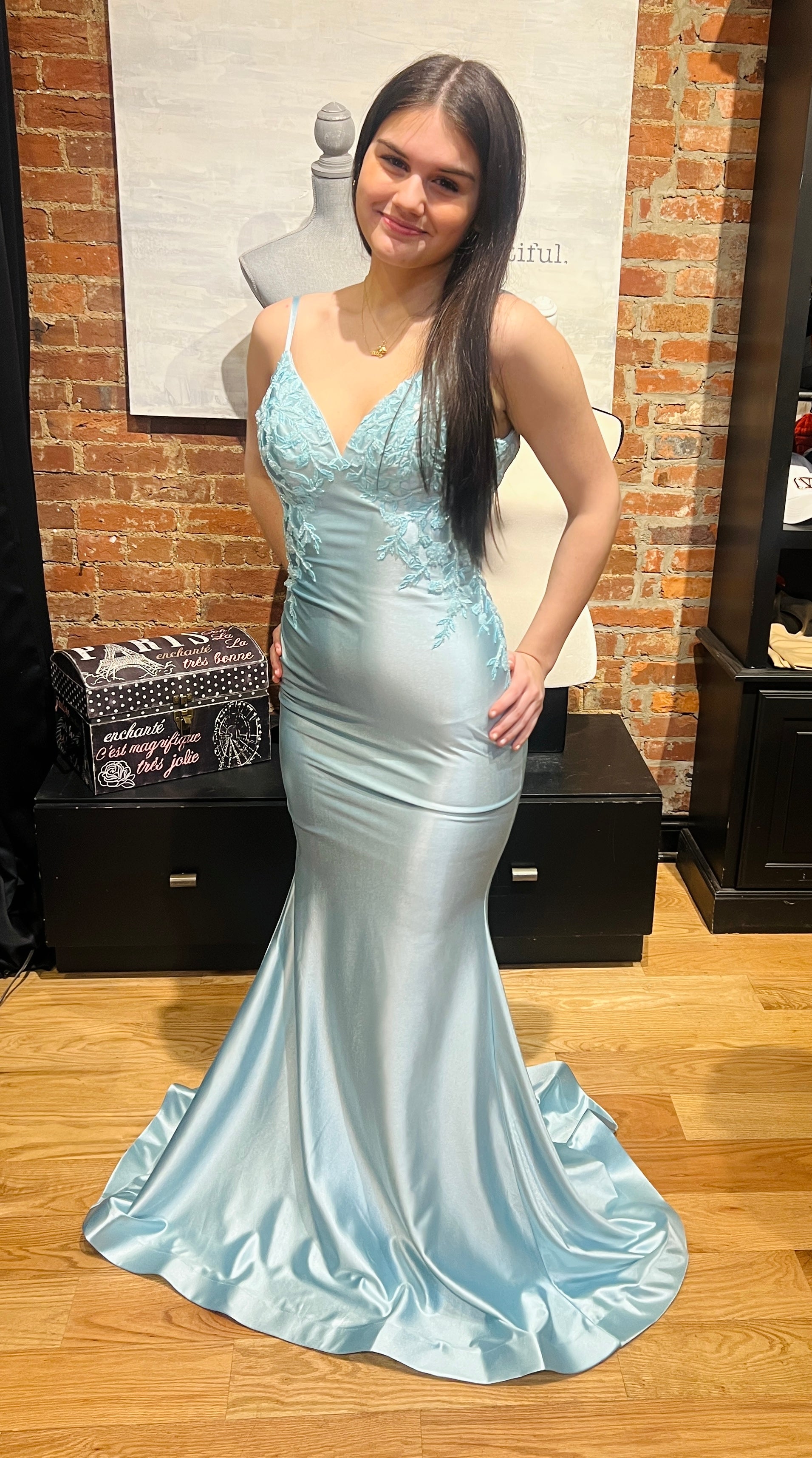 Woman in a light blue evening gown standing in front of a brick wall.