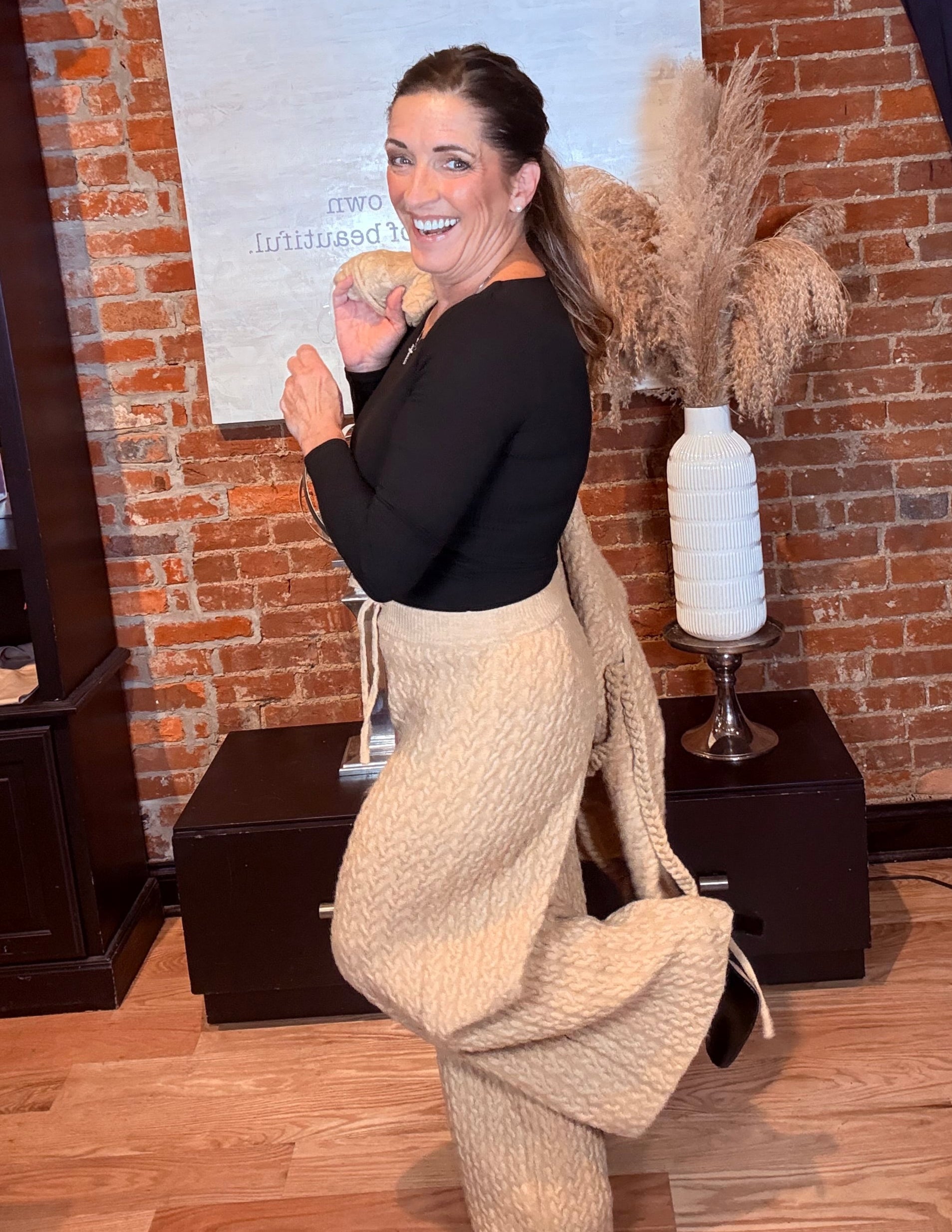 Woman standing in a room with brick walls and wooden floor, holding a bottle.
