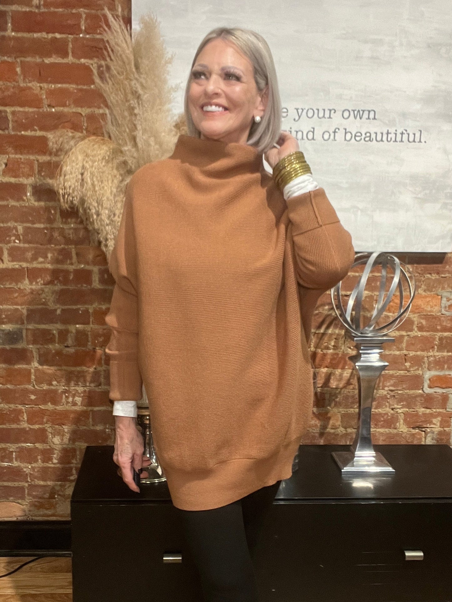 Woman in a brown sweater standing next to a piano with a brick wall background