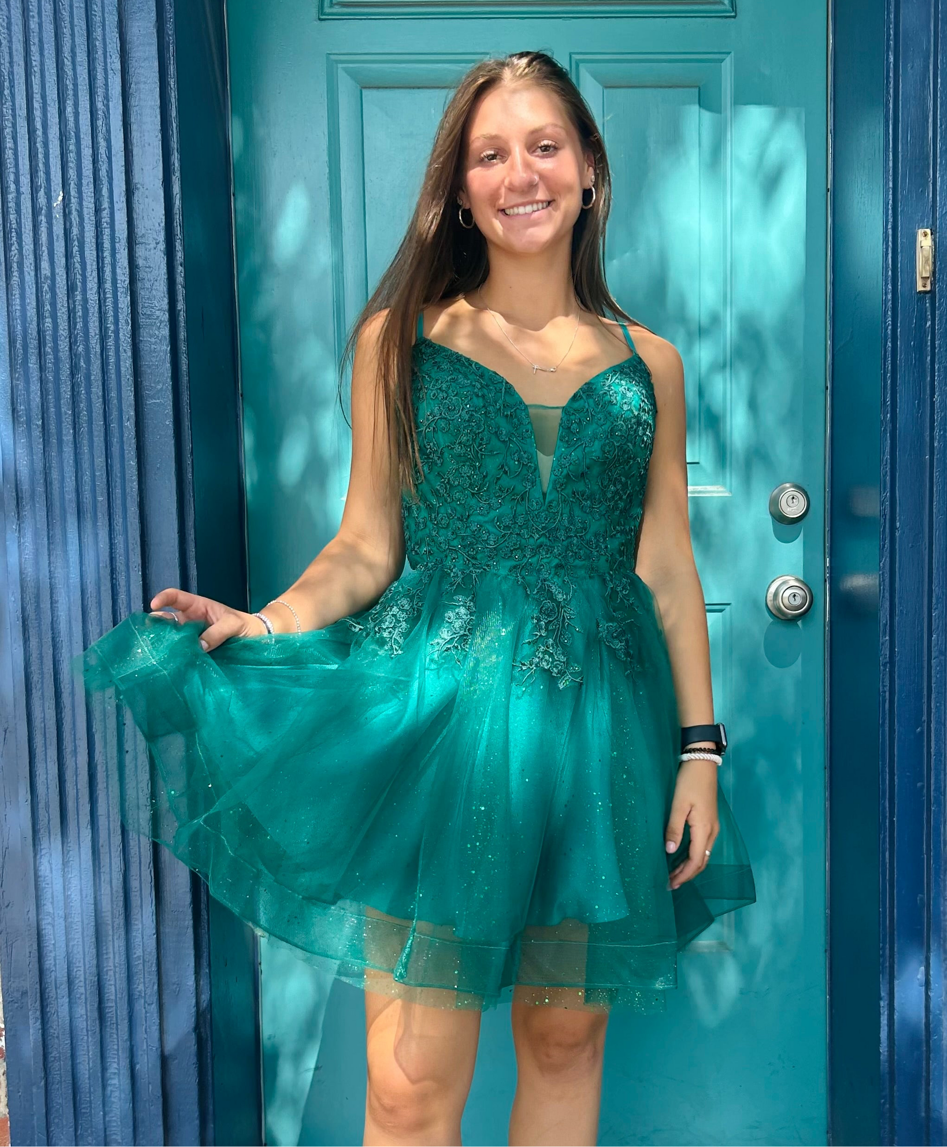A girl wearing a green sparkling homecoming dress with glitter and fairytale details, standing in front of a blue door.