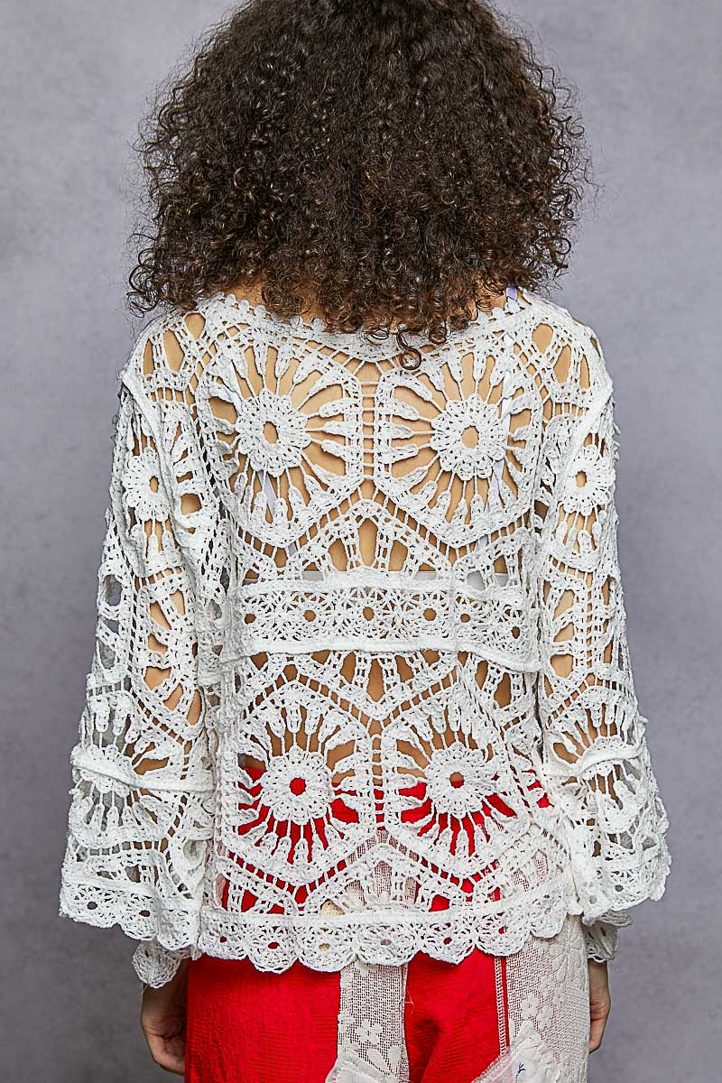 Person wearing a white crochet top with red pants on a gray background