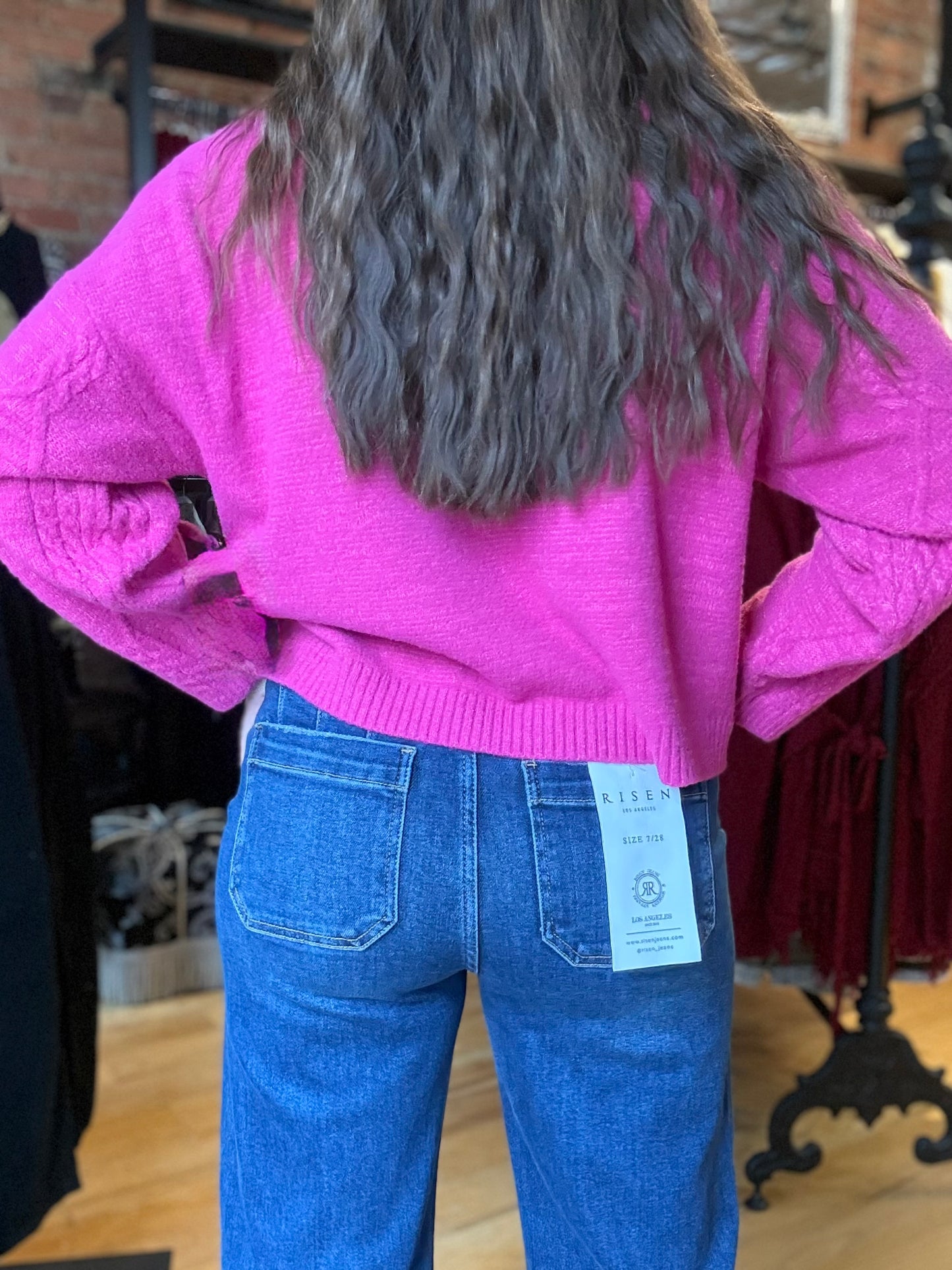Person wearing a pink sweater and blue jeans with a visible tag, standing in a store setting.