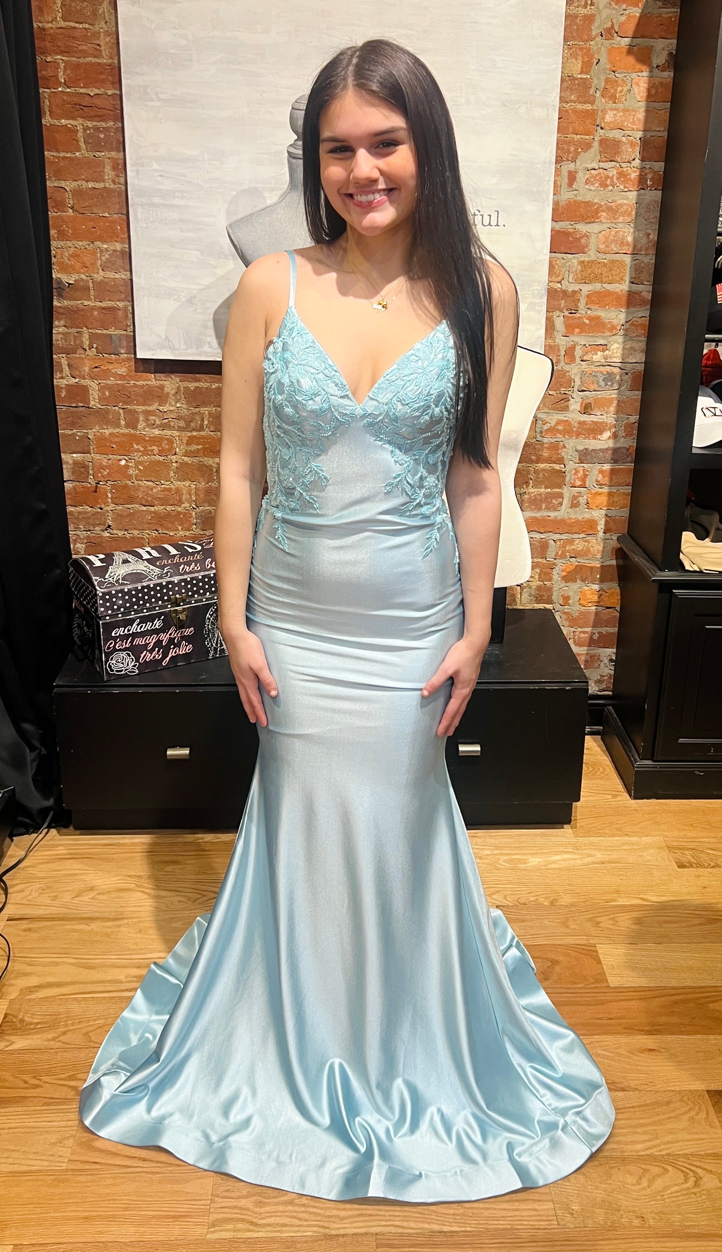 Woman in a light blue evening gown standing in front of a brick wall.