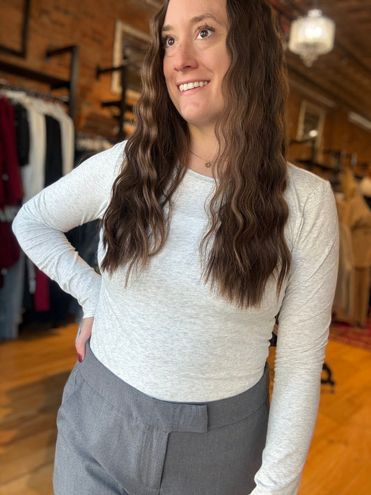 Woman wearing a white long-sleeve top and gray pants in a clothing store.