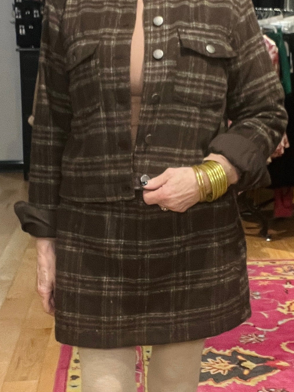 Person wearing a brown plaid coat with visible buttons, standing on a patterned rug.