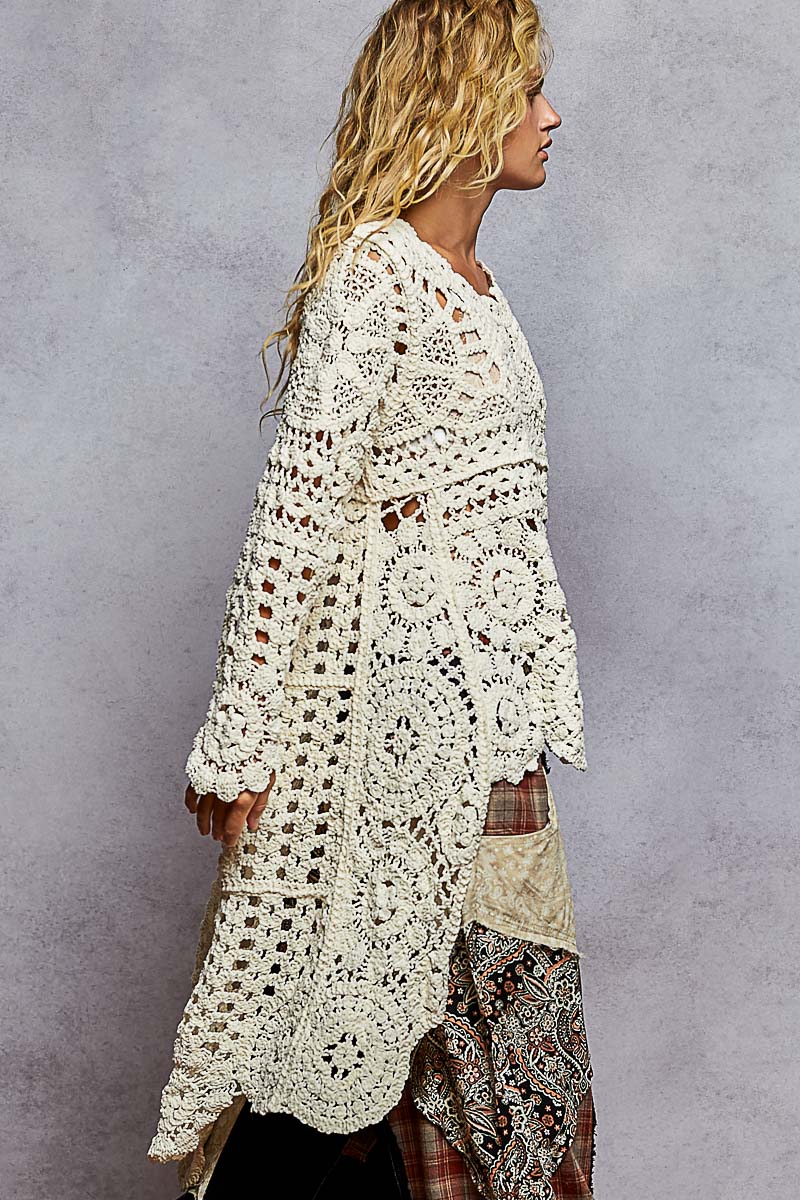 Woman wearing a white crochet cardigan against a gray background