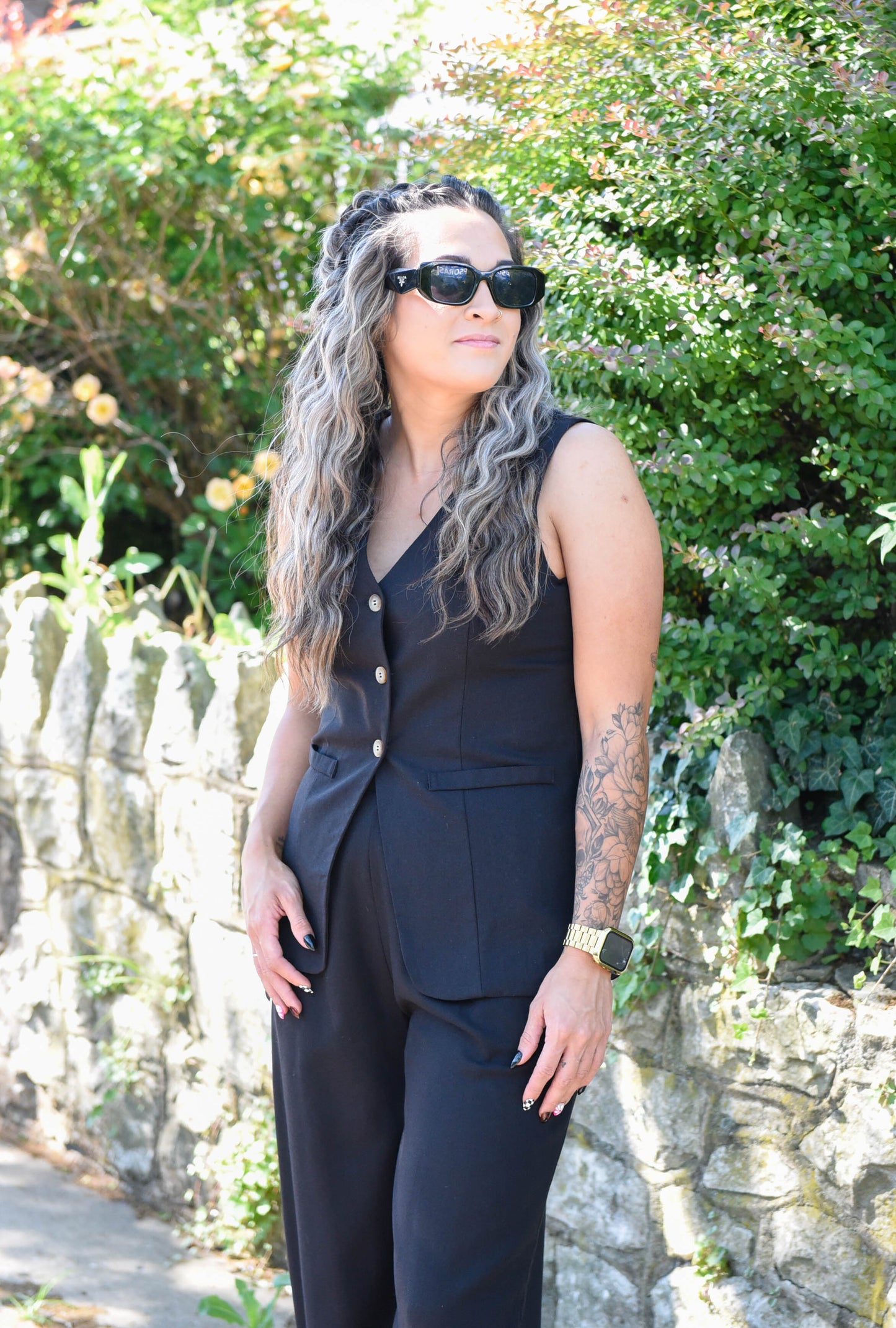 Woman in a black outfit standing outdoors with greenery in the background