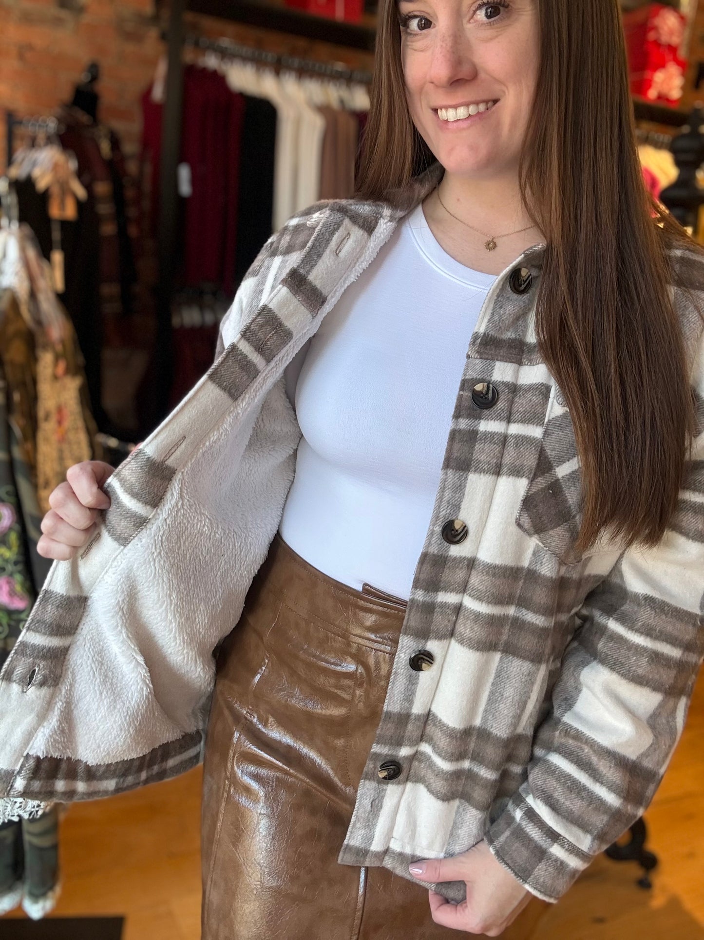 Woman wearing a plaid jacket over a white top and brown pants in a clothing store.