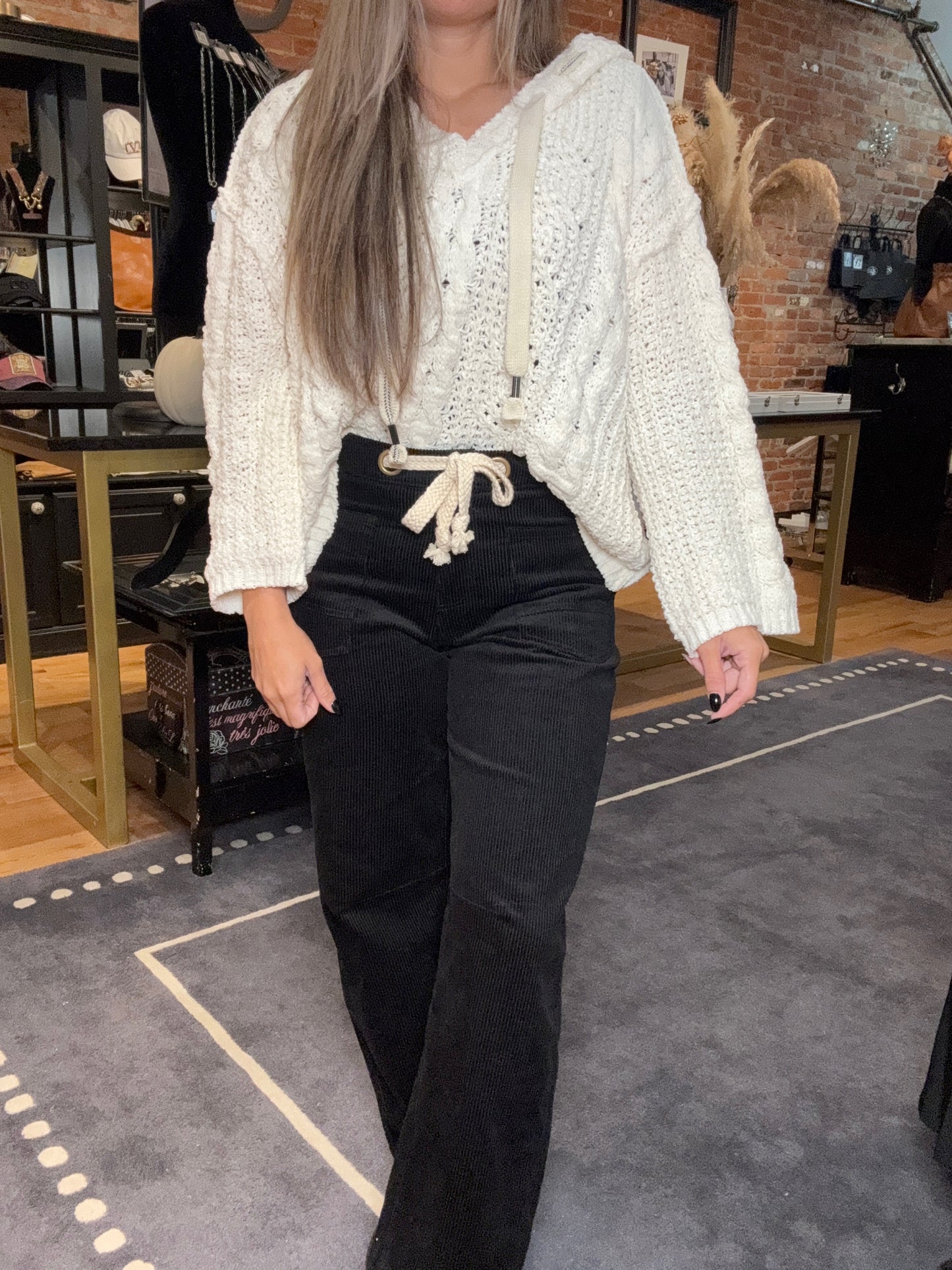 Person wearing a white sweater and black pants in an indoor setting