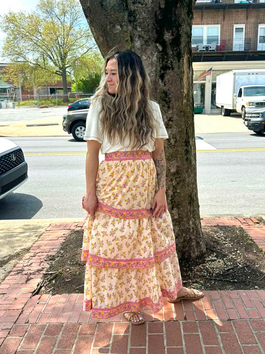 Woman in a floral dress standing on a sidewalk next to a tree