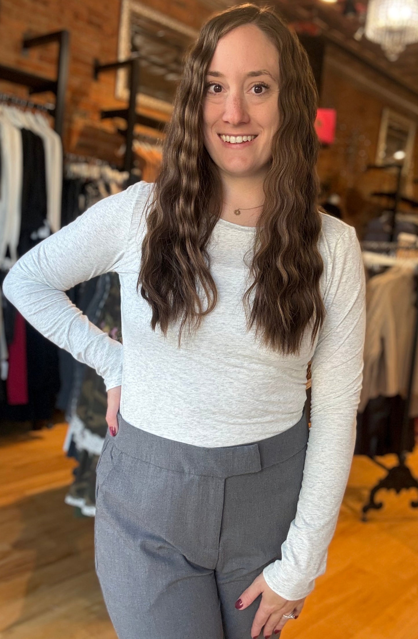 Woman in a white long-sleeve top and gray pants standing in a clothing store.