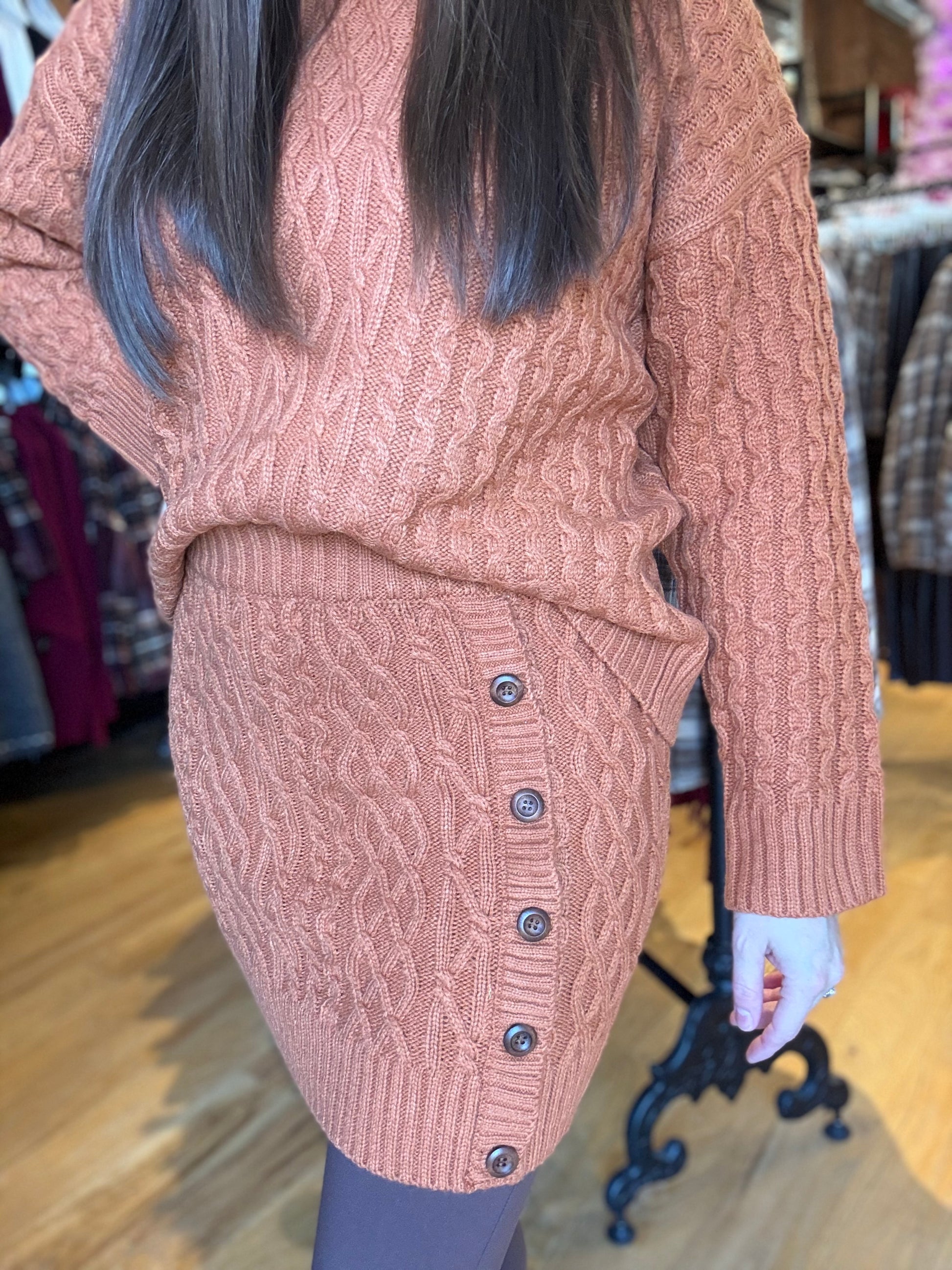 Person wearing a pink cable knit sweater and skirt set in a store setting.