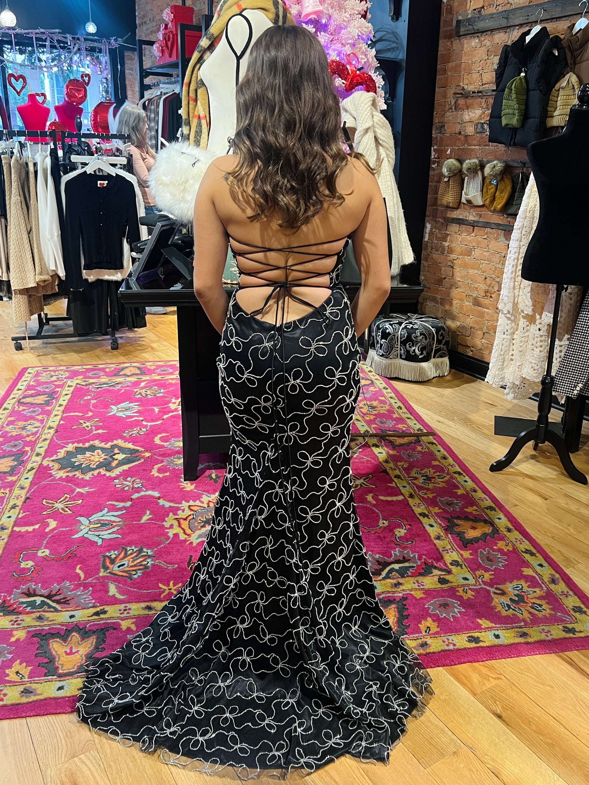 Woman wearing a black dress with intricate white patterns in a clothing store.
