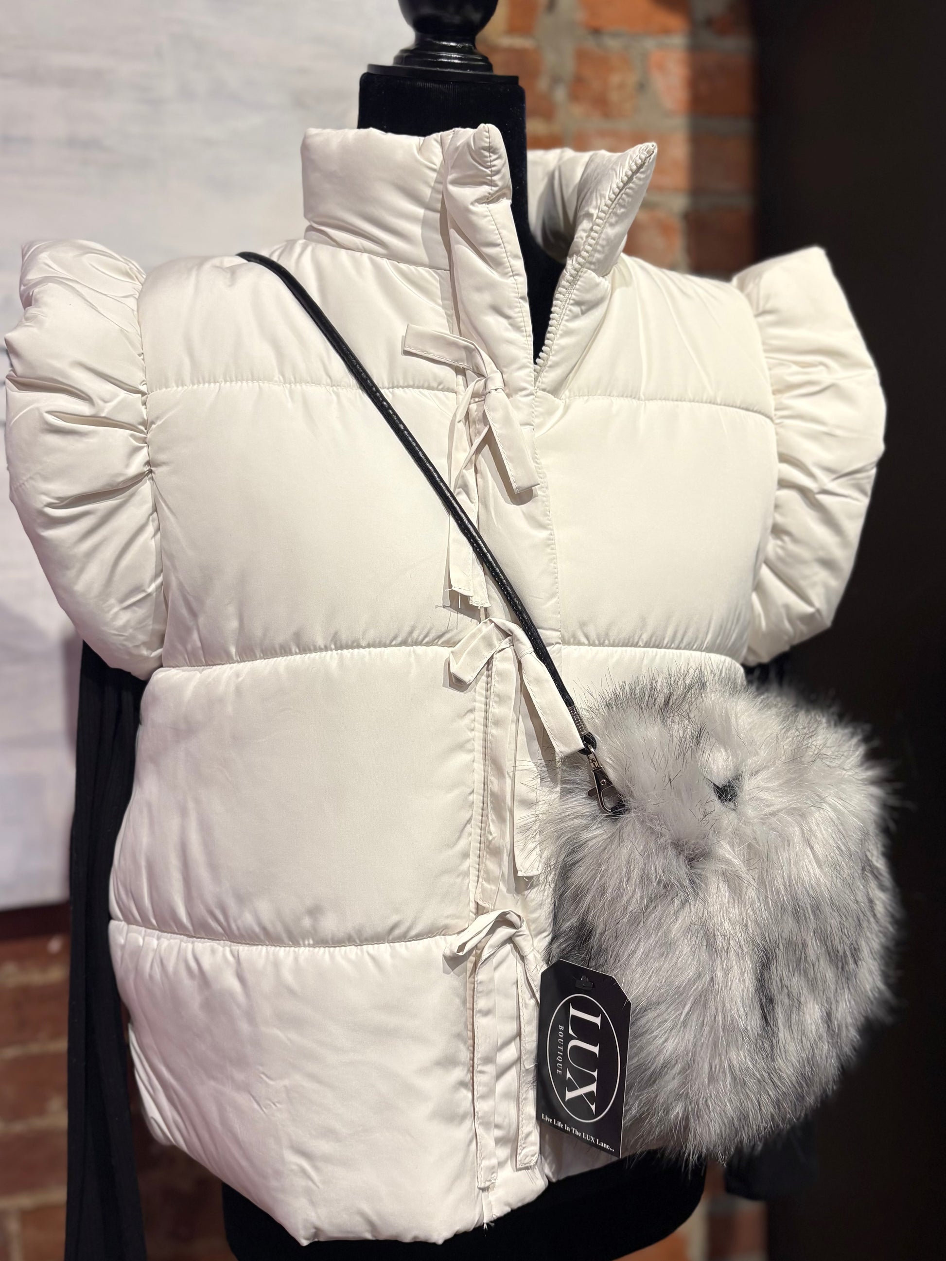 White puffer vest with fur hood on a mannequin against a brick wall background
