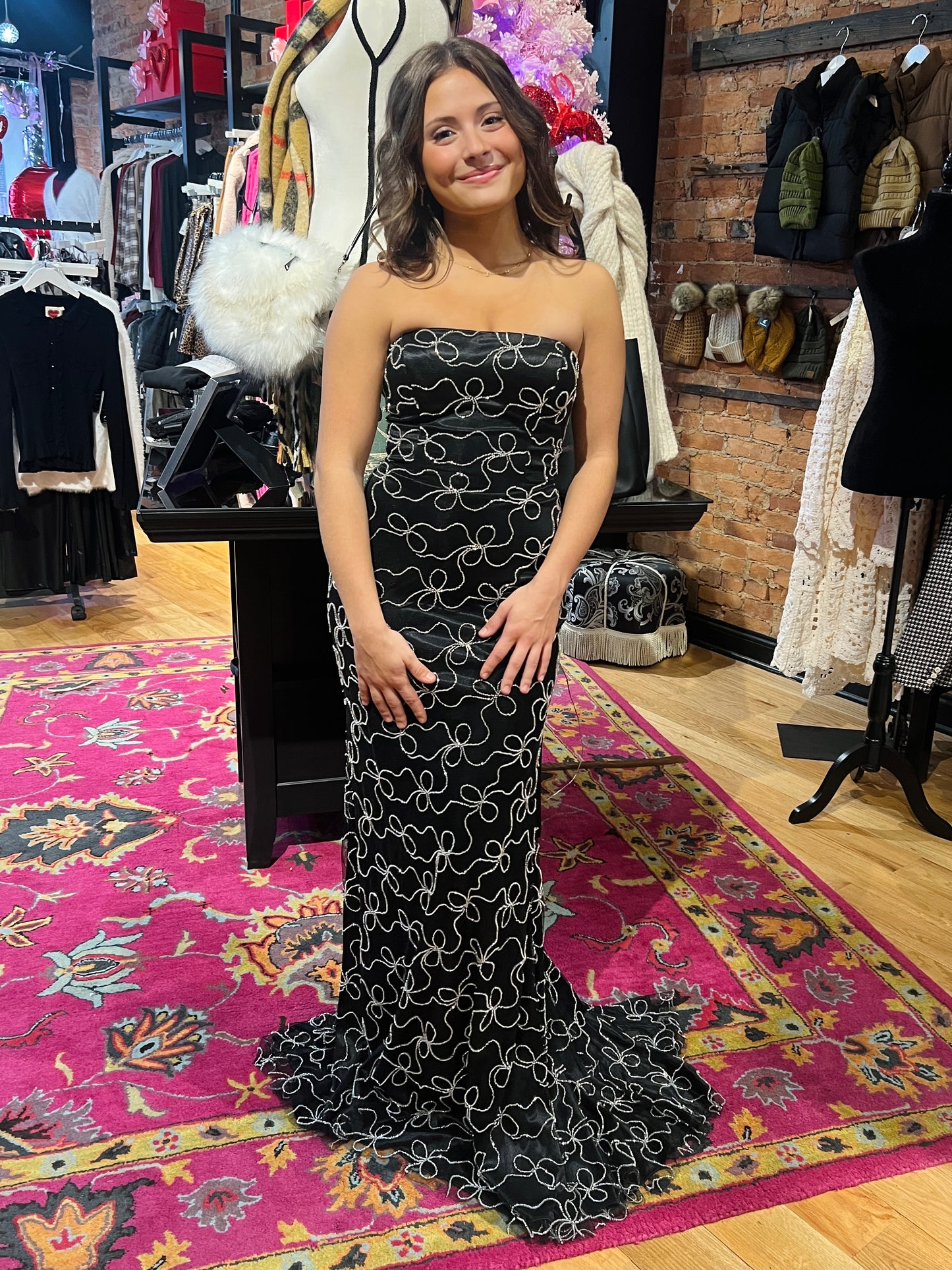 Woman in a strapless black and white patterned gown standing on a colorful rug in a clothing store.