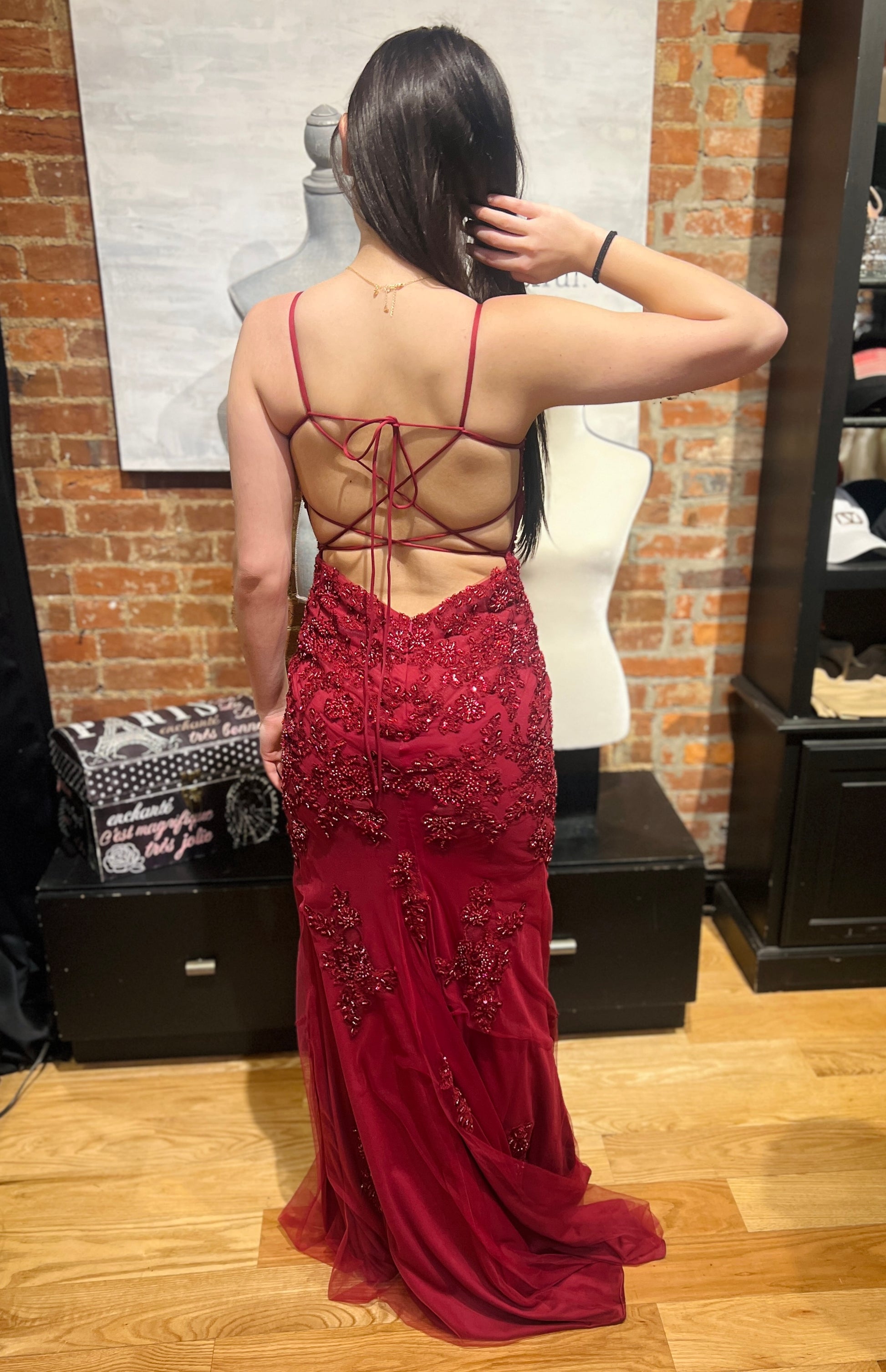 Woman wearing a red evening gown with intricate back design in a room with brick walls.