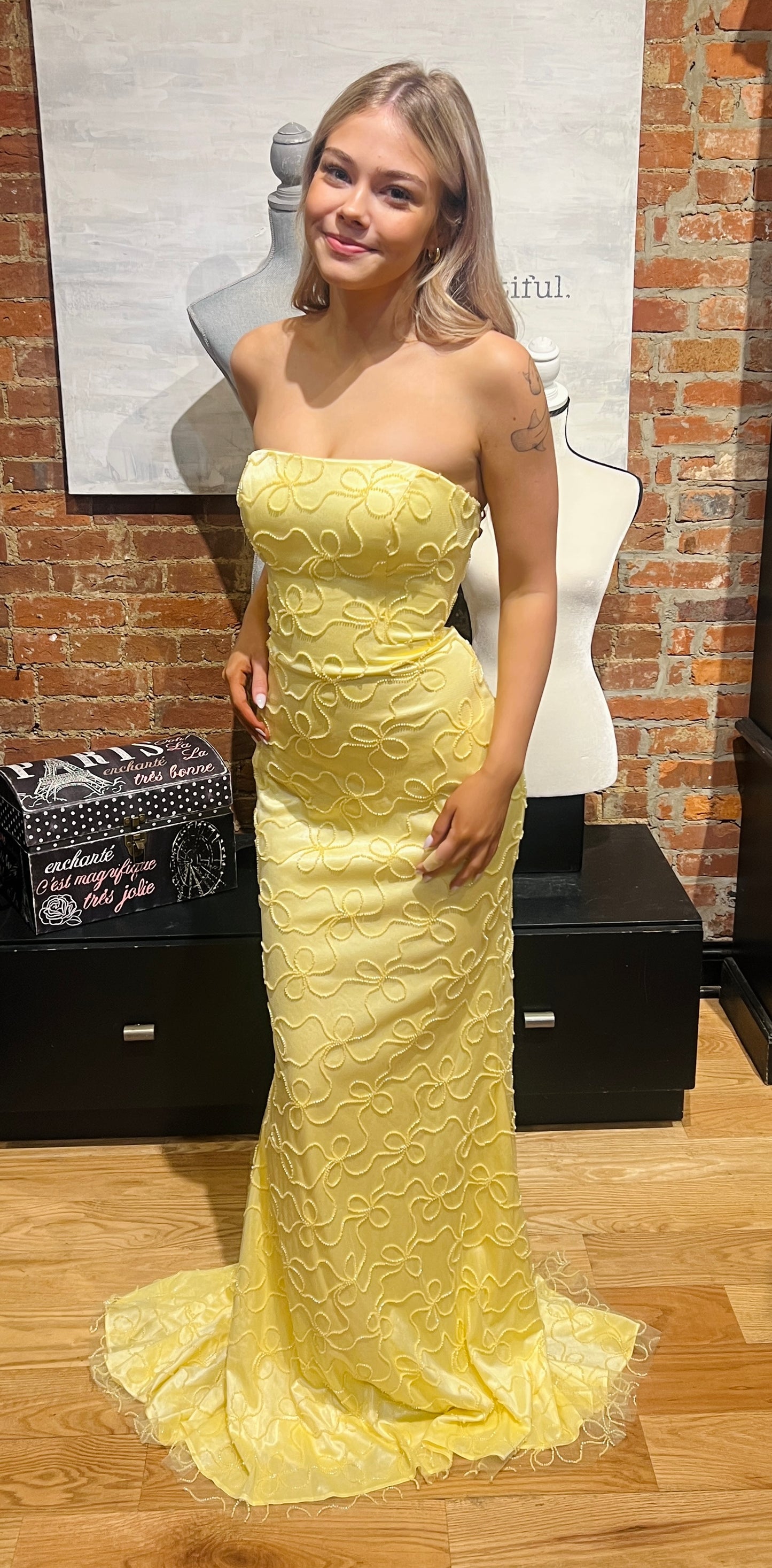 Woman wearing a yellow strapless dress in front of a brick wall.