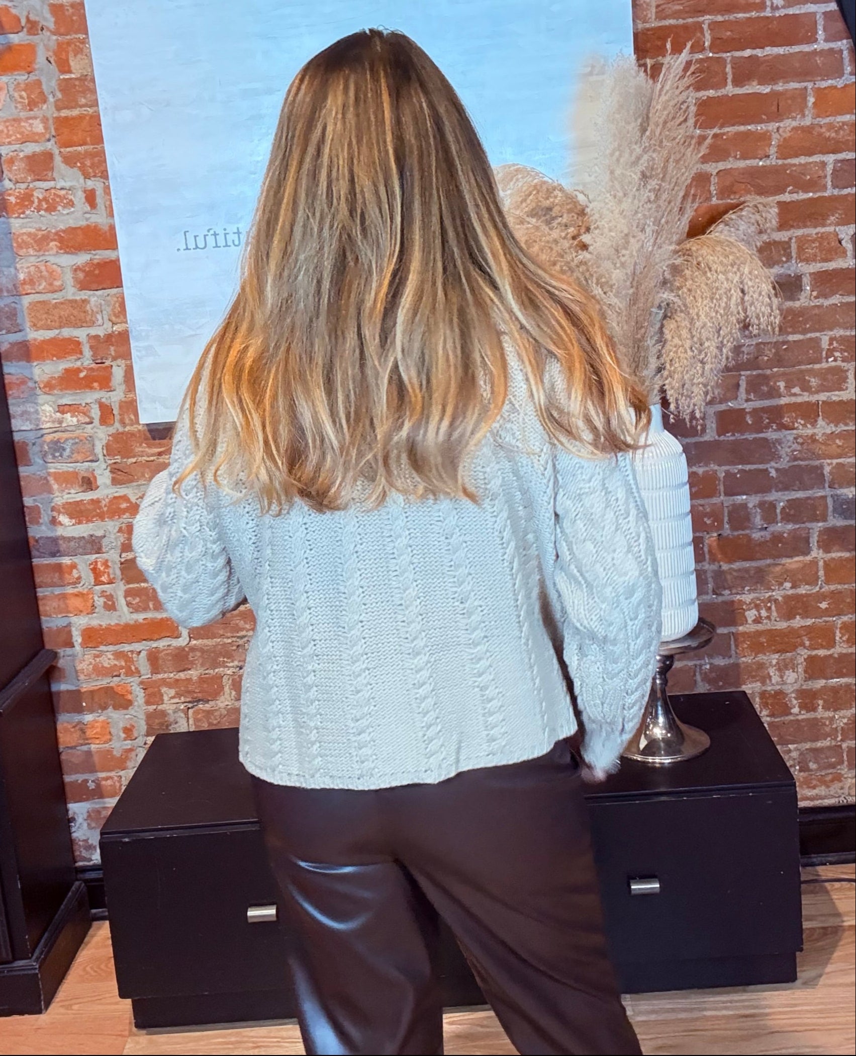 Person wearing a white sweater and brown leather pants standing on a wooden floor.