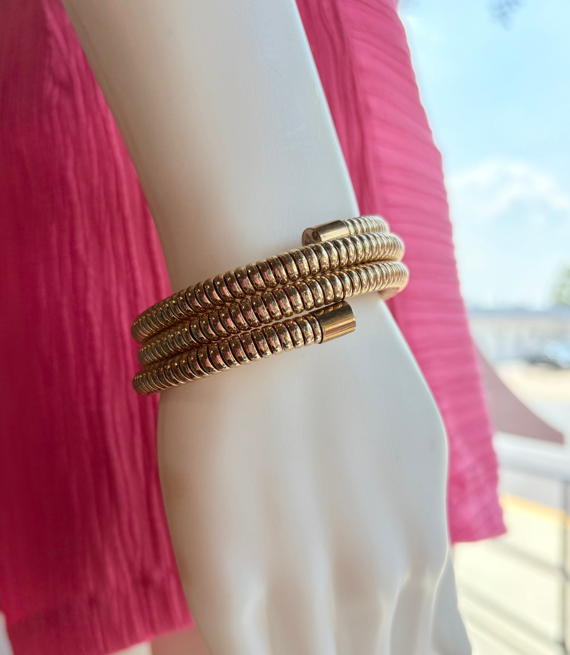 Close-up of a person wearing a stack of gold bracelets with a blurred outdoor background.