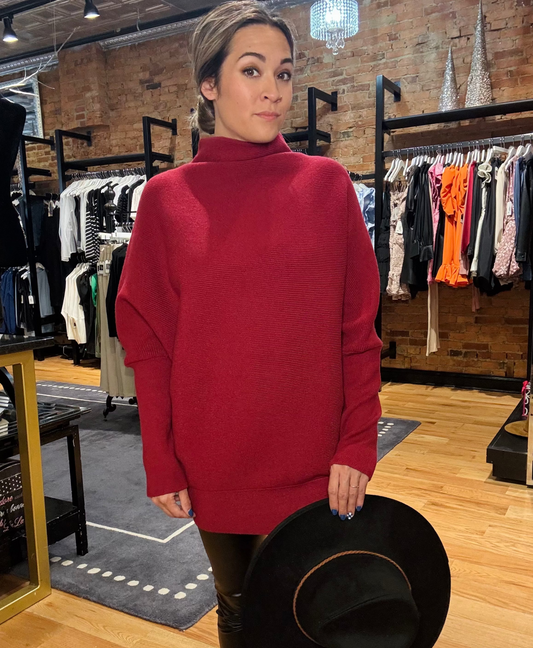Woman wearing a red sweater holding a black hat in a clothing store.