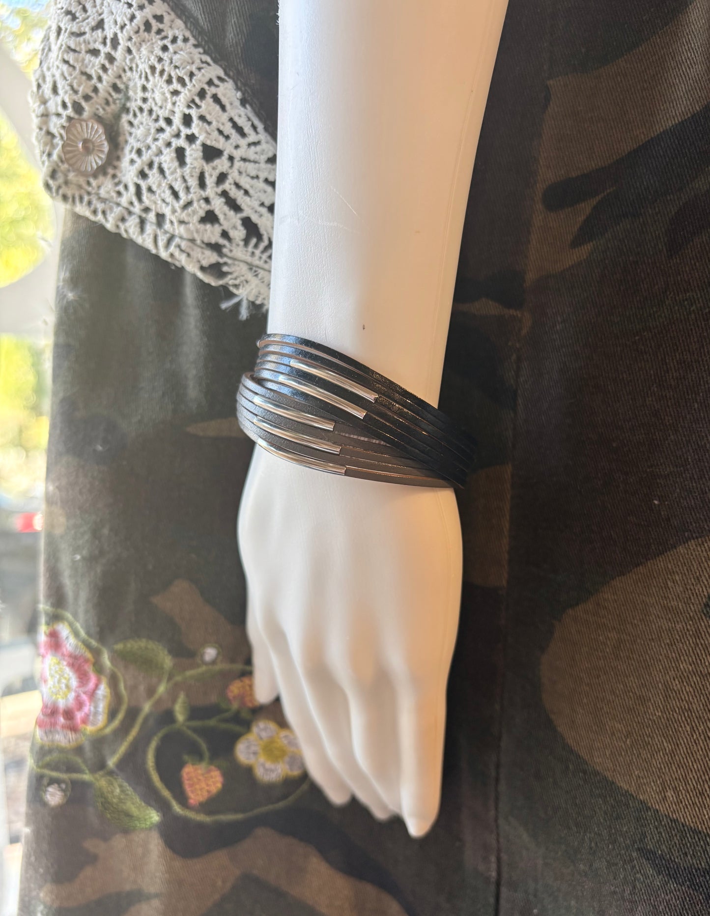 Mannequin hand wearing a black bracelet with a camouflage-patterned garment in the background