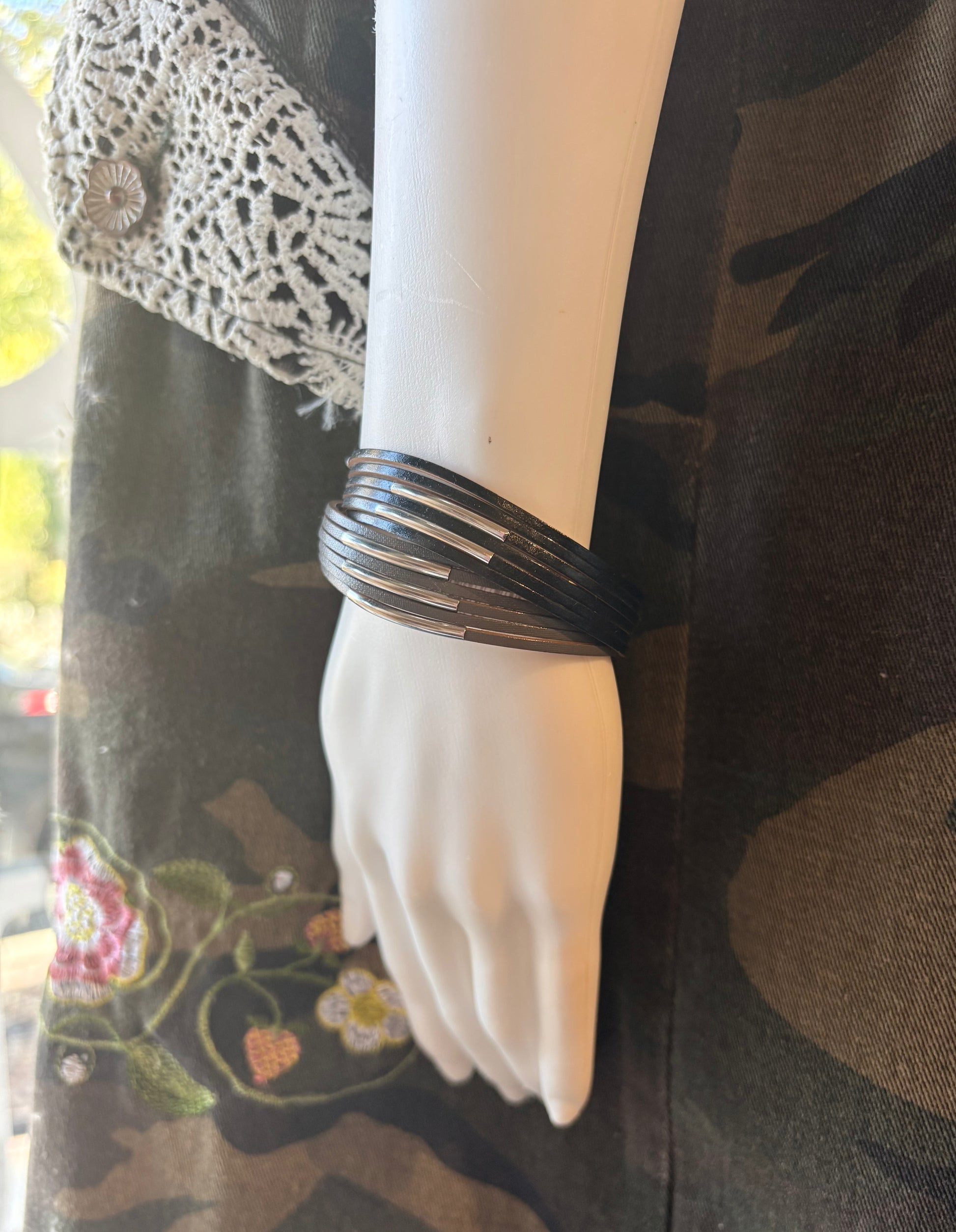 Mannequin hand wearing a black bracelet with a camouflage-patterned garment in the background