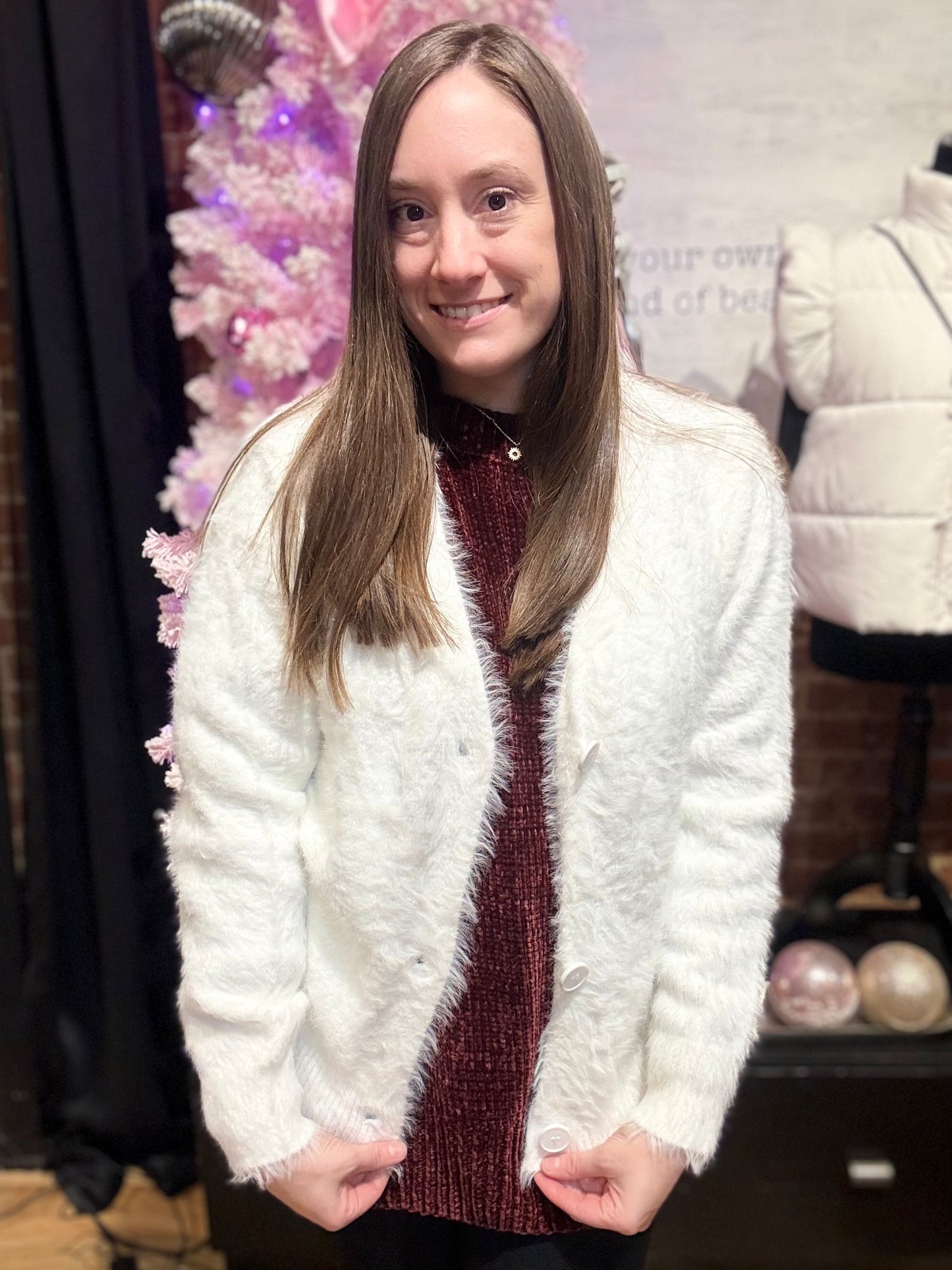 Woman wearing a white fluffy jacket over a red sweater in front of a decorated Christmas tree.