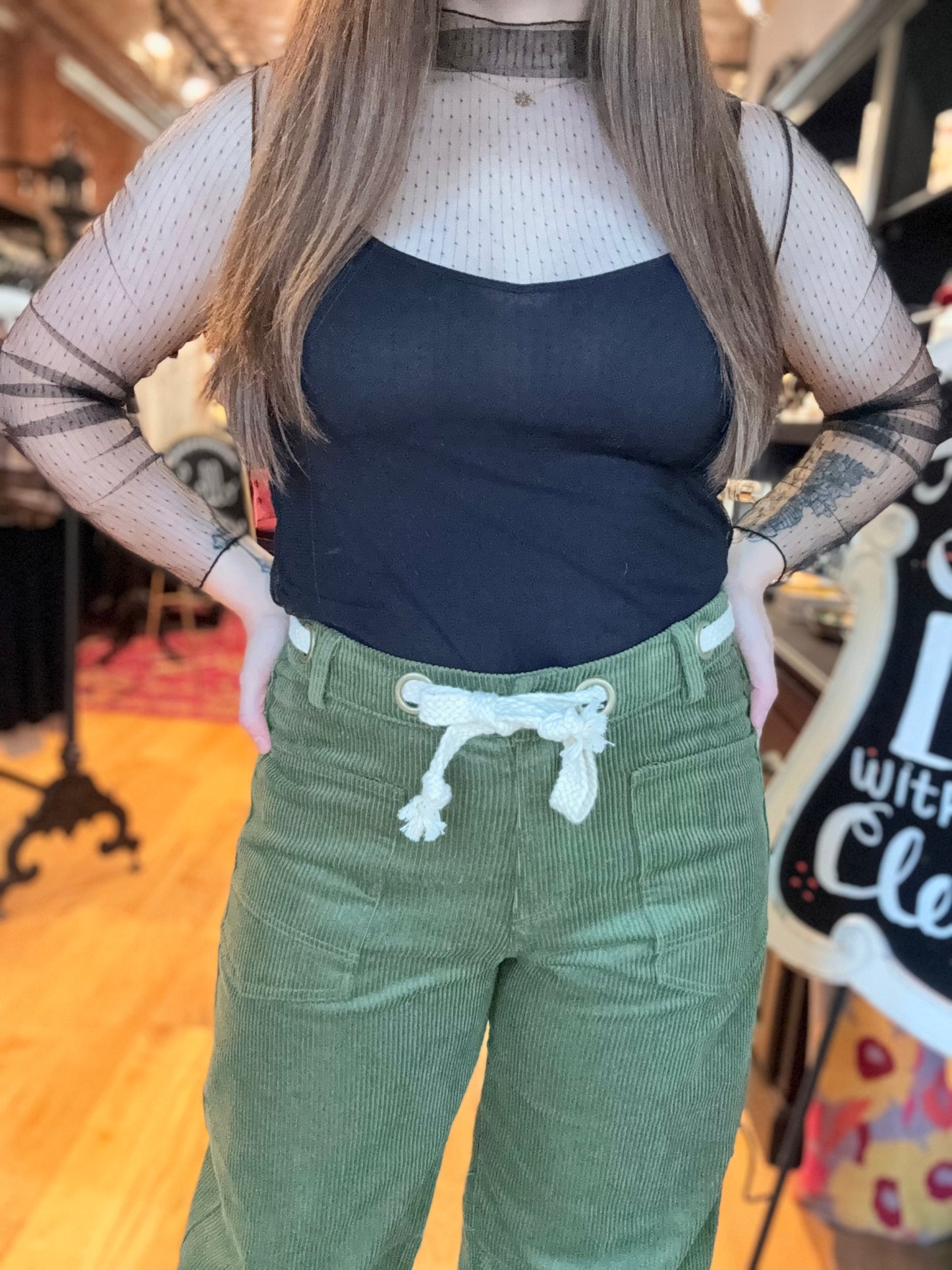 Person wearing a black top and green pants with a white design, standing indoors.