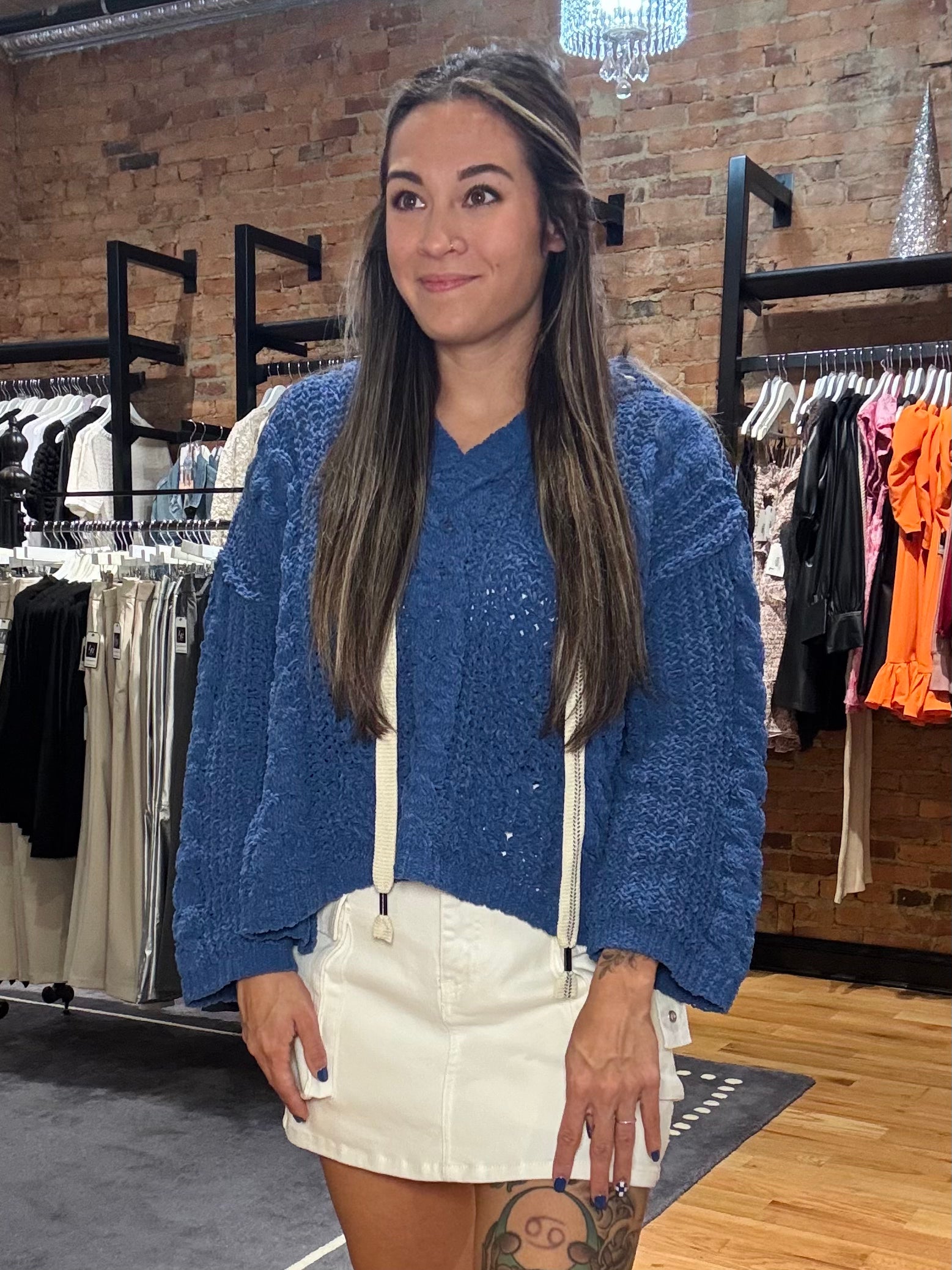 Woman wearing a blue sweater and white skirt in a clothing store.
