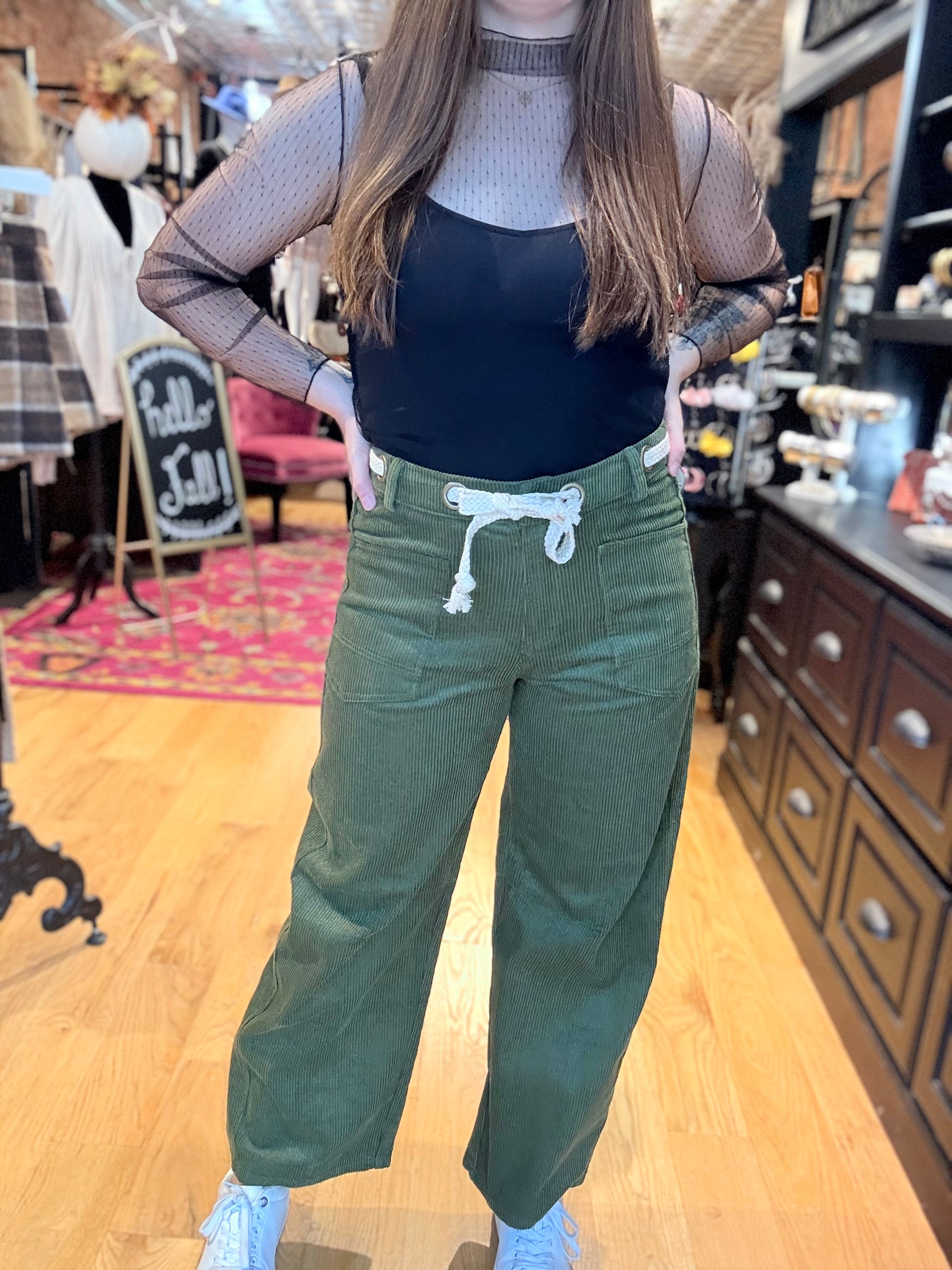 Person wearing a black top and green pants in a store setting