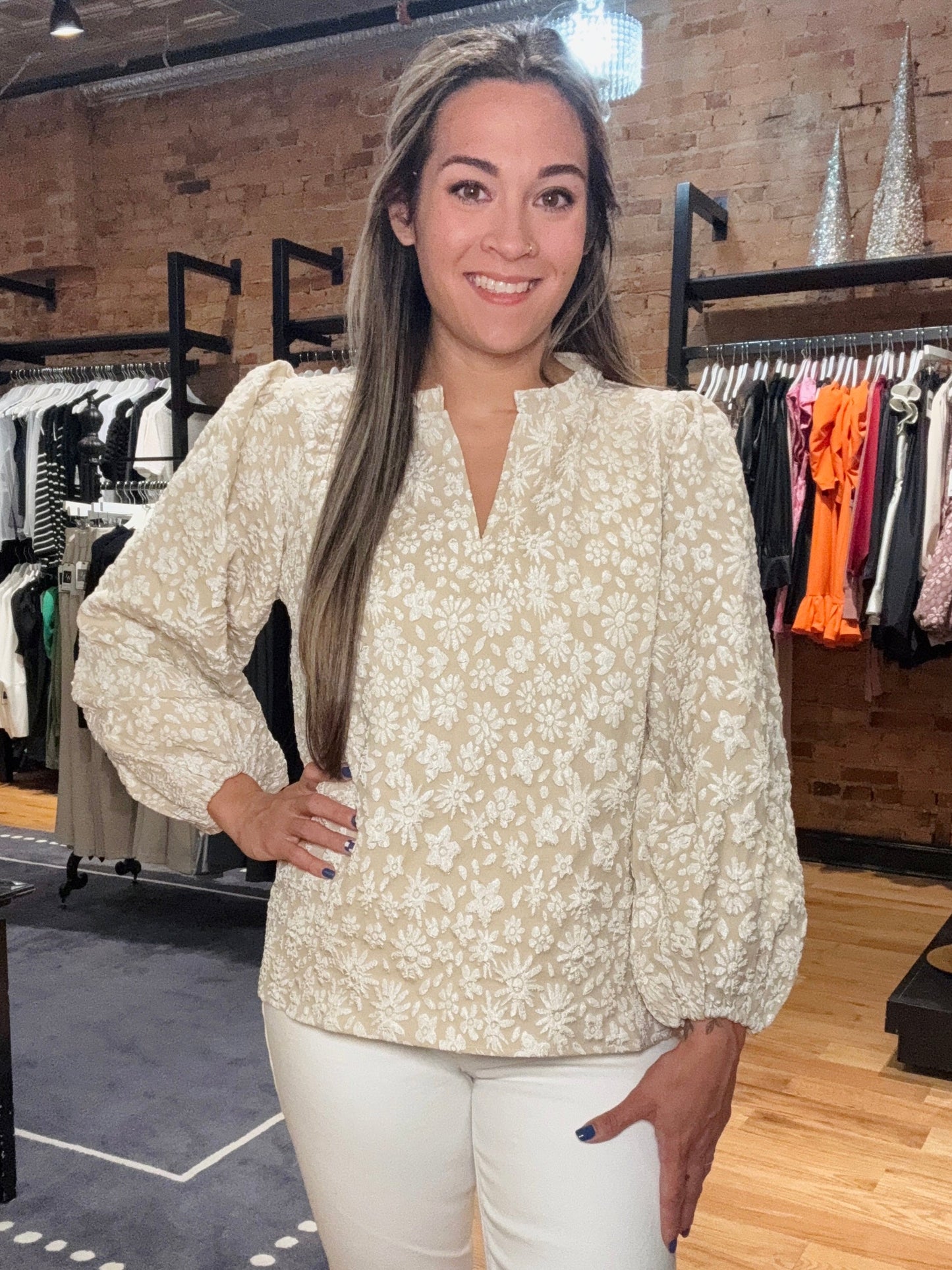Woman in a floral blouse and white pants standing in a clothing store.