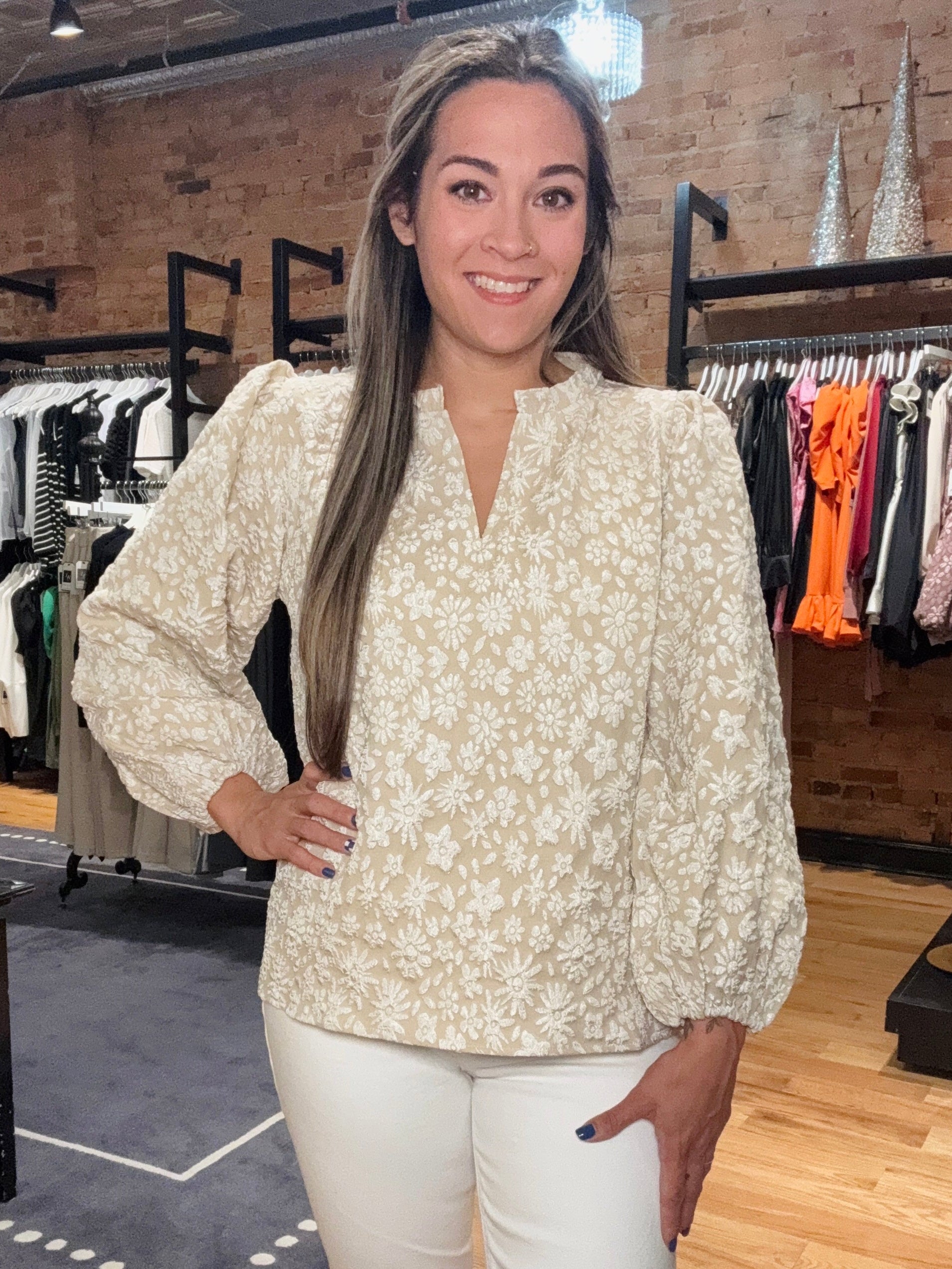 Woman in a floral blouse and white pants standing in a clothing store.