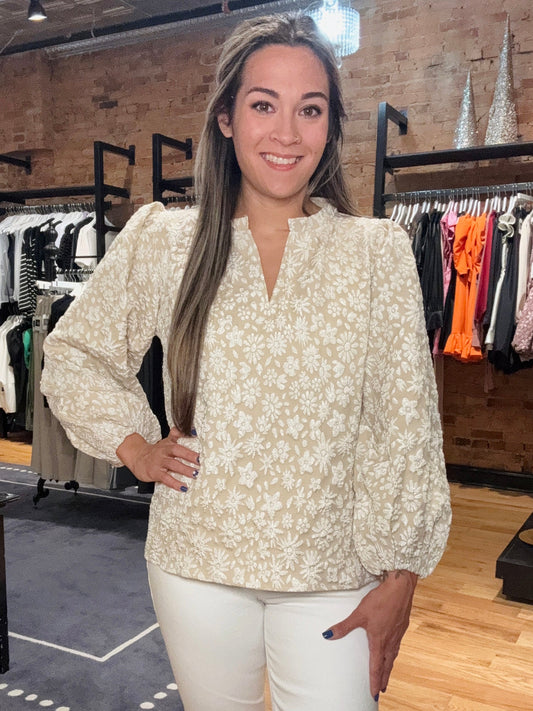 Woman in a floral blouse and white pants standing in a clothing store.