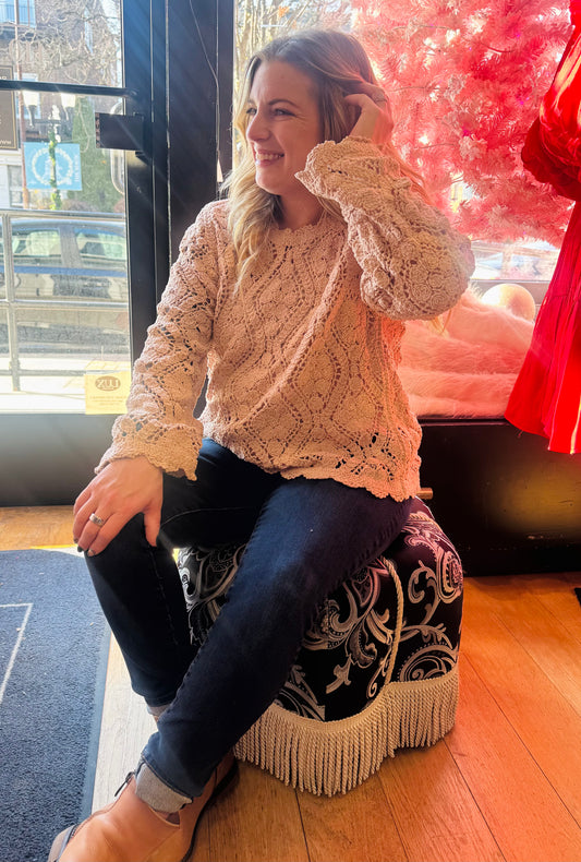 Woman sitting on a decorative stool indoors, wearing a textured sweater.