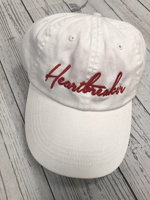 White cap with 'Heartbreaker' embroidery on a wooden surface