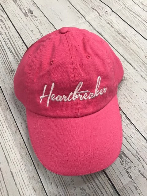 Red cap with 'Heartbreaker' embroidery on a wooden surface